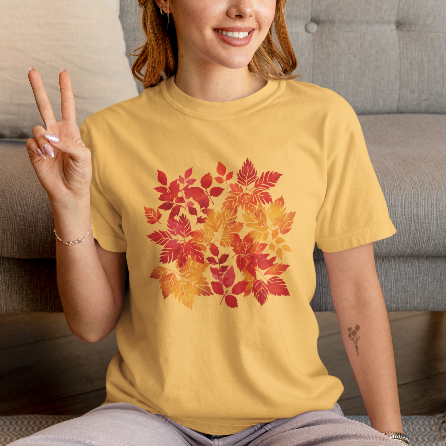 Person wearing a yellow t-shirt with autumn leaf design, sitting on a couch.