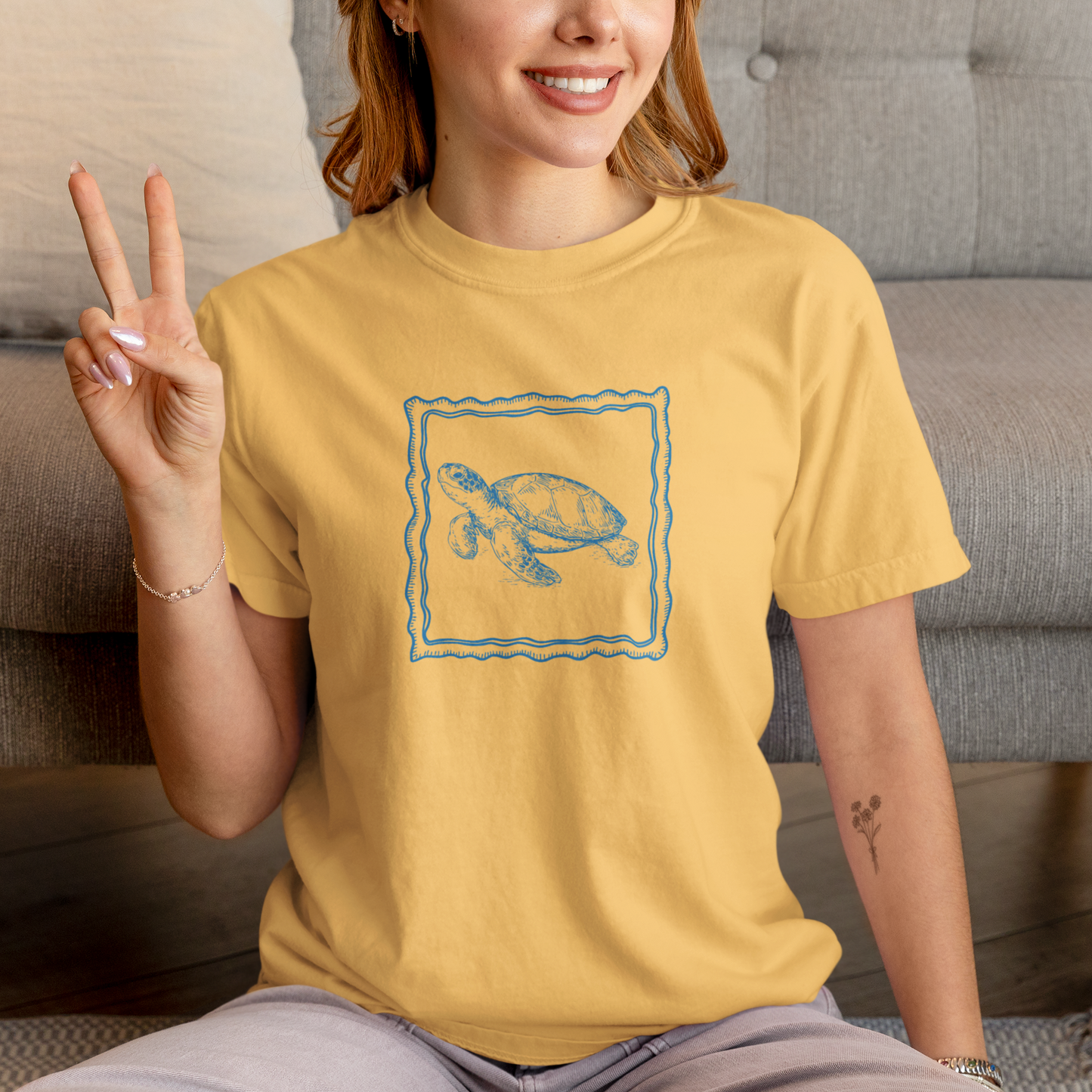 Person wearing a yellow t-shirt with a turtle design, sitting on the floor.