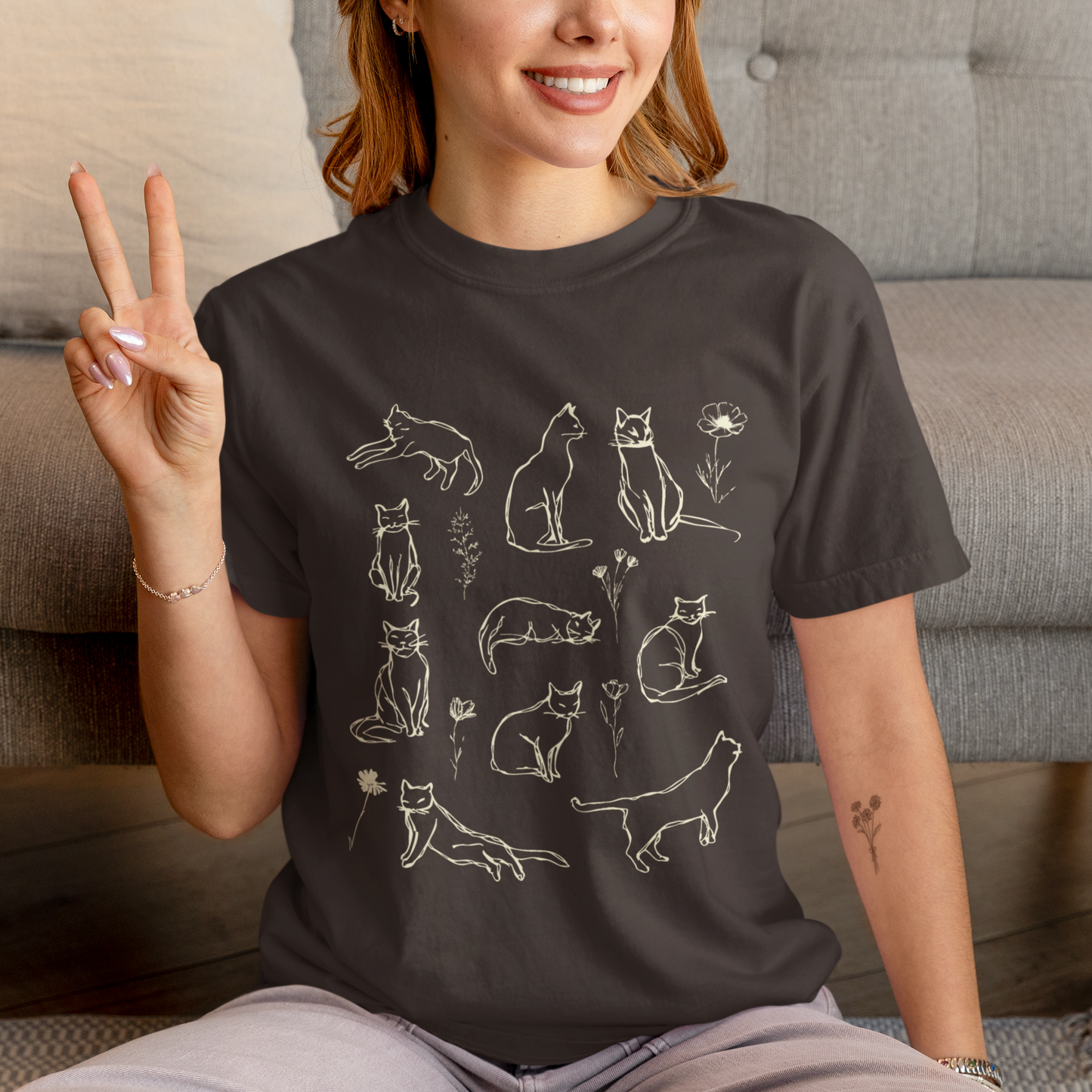 Person wearing a black t-shirt with cat illustrations, sitting on a couch.