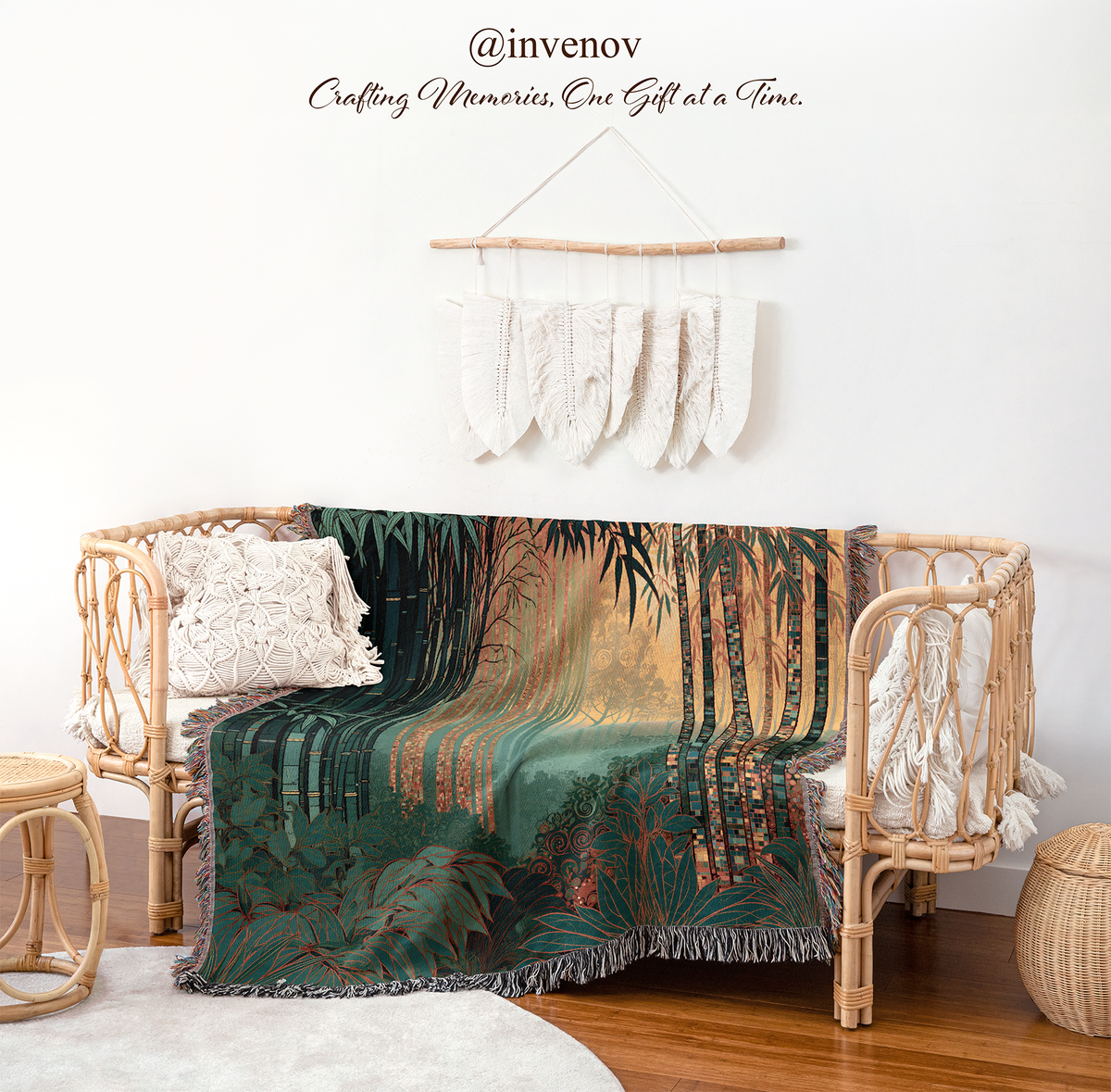 A woven rattan daybed styled in a boho room setting, draped with a dark green and gold tropical forest patterned throw blanket. The scene includes a white wall with macrame wall hanging, wooden floor, a small woven stool, and a round basket.