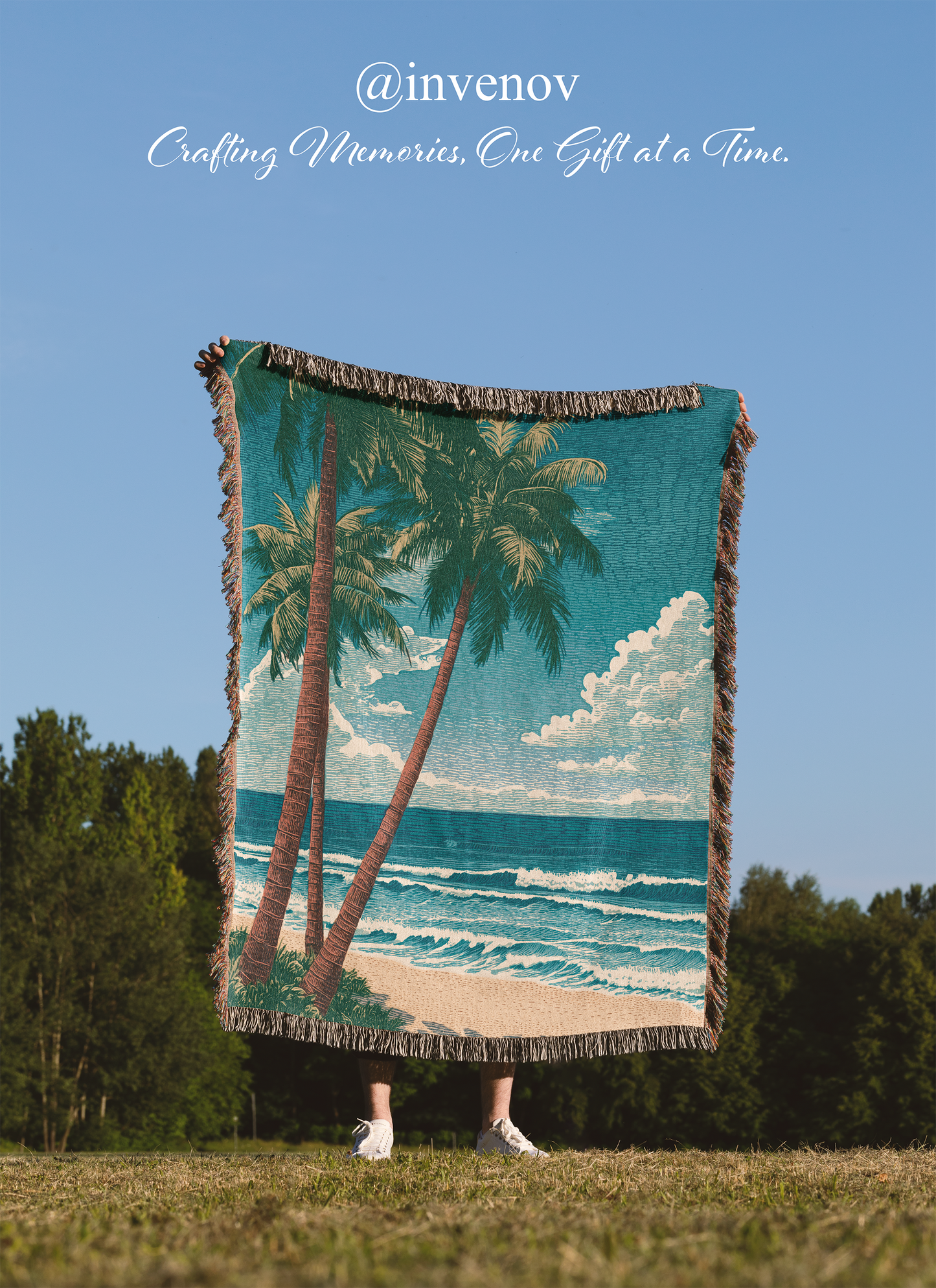 Person holding a beach-themed blanket with palm trees and ocean on a grassy field.