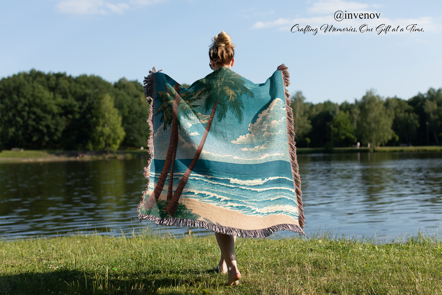 Person holding a woven blanket with beach with palm tree design by a lake