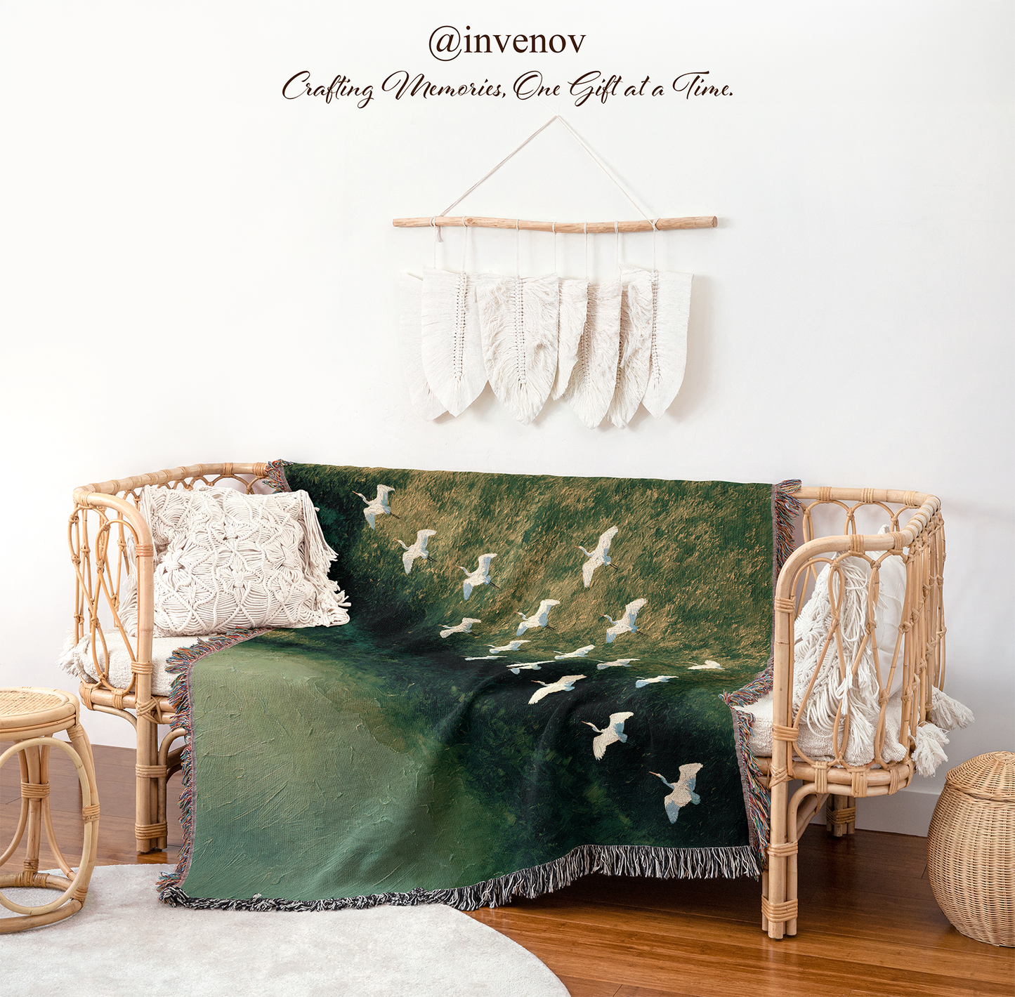 A woven throw blanket draped over a rattan daybed in a styled room. The blanket features a dark green background with a white crisscross pattern and white birds in flight.