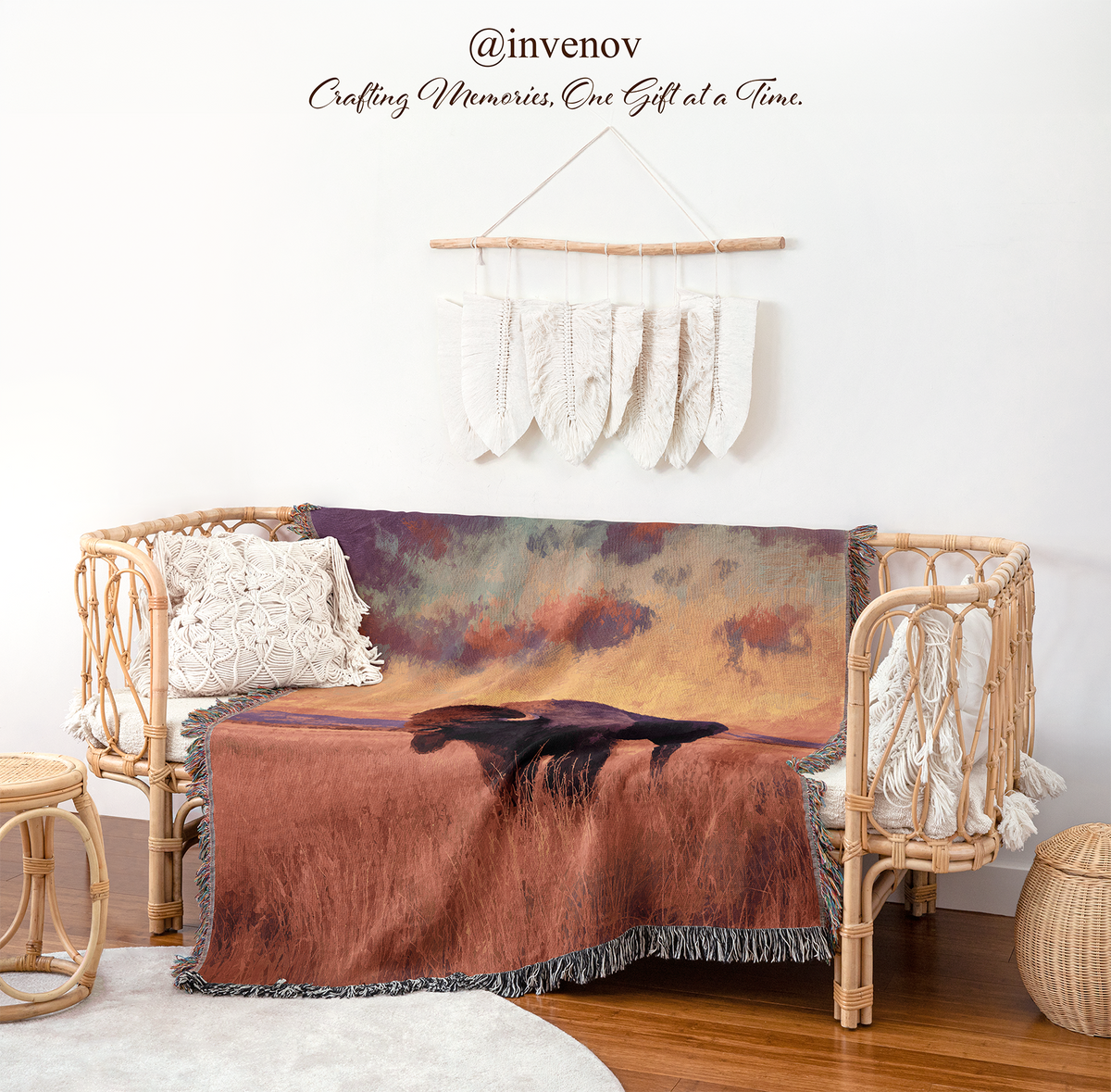 A woven rattan daybed styled in a bohemian nursery setting, draped with a large printed blanket featuring a sunset landscape and a dark horse silhouette. The room includes a white wall with a macrame wall hanging, a wooden stool, and a round rug.