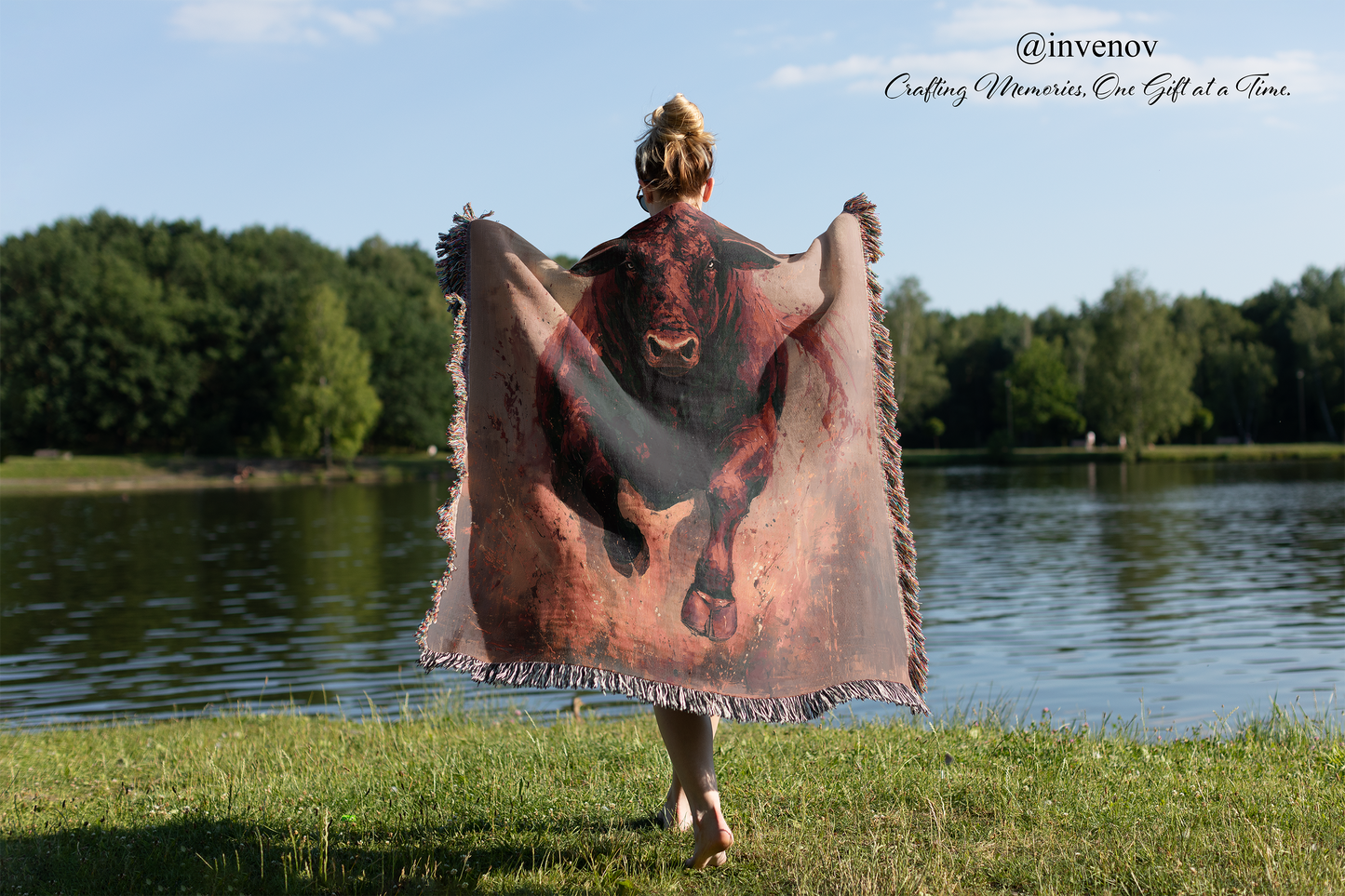 Person holding a blanket with bull design by a lake