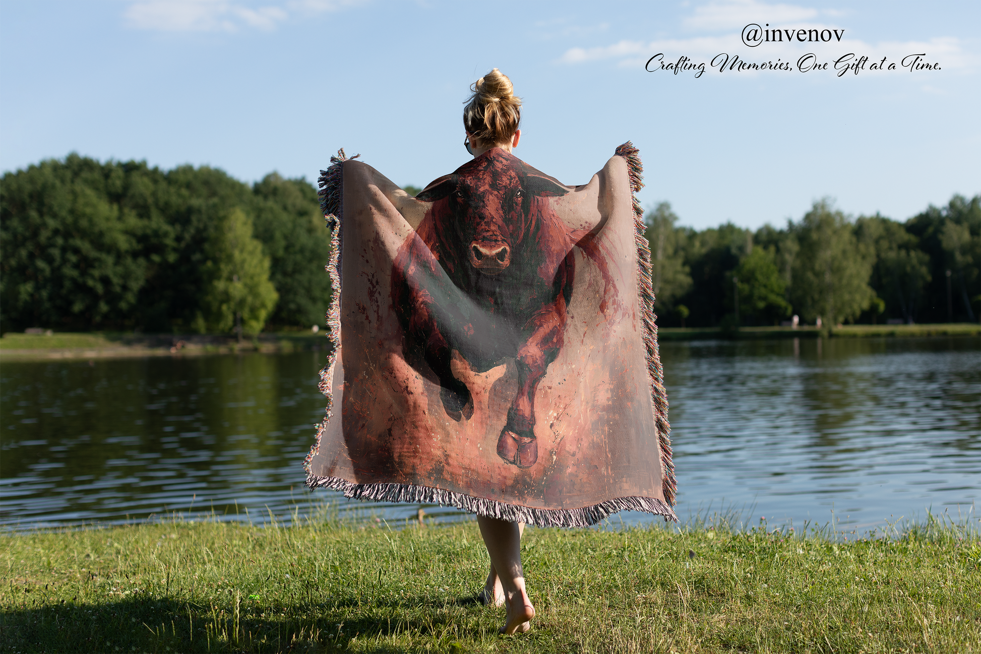 Person holding a blanket with bull design by a lake