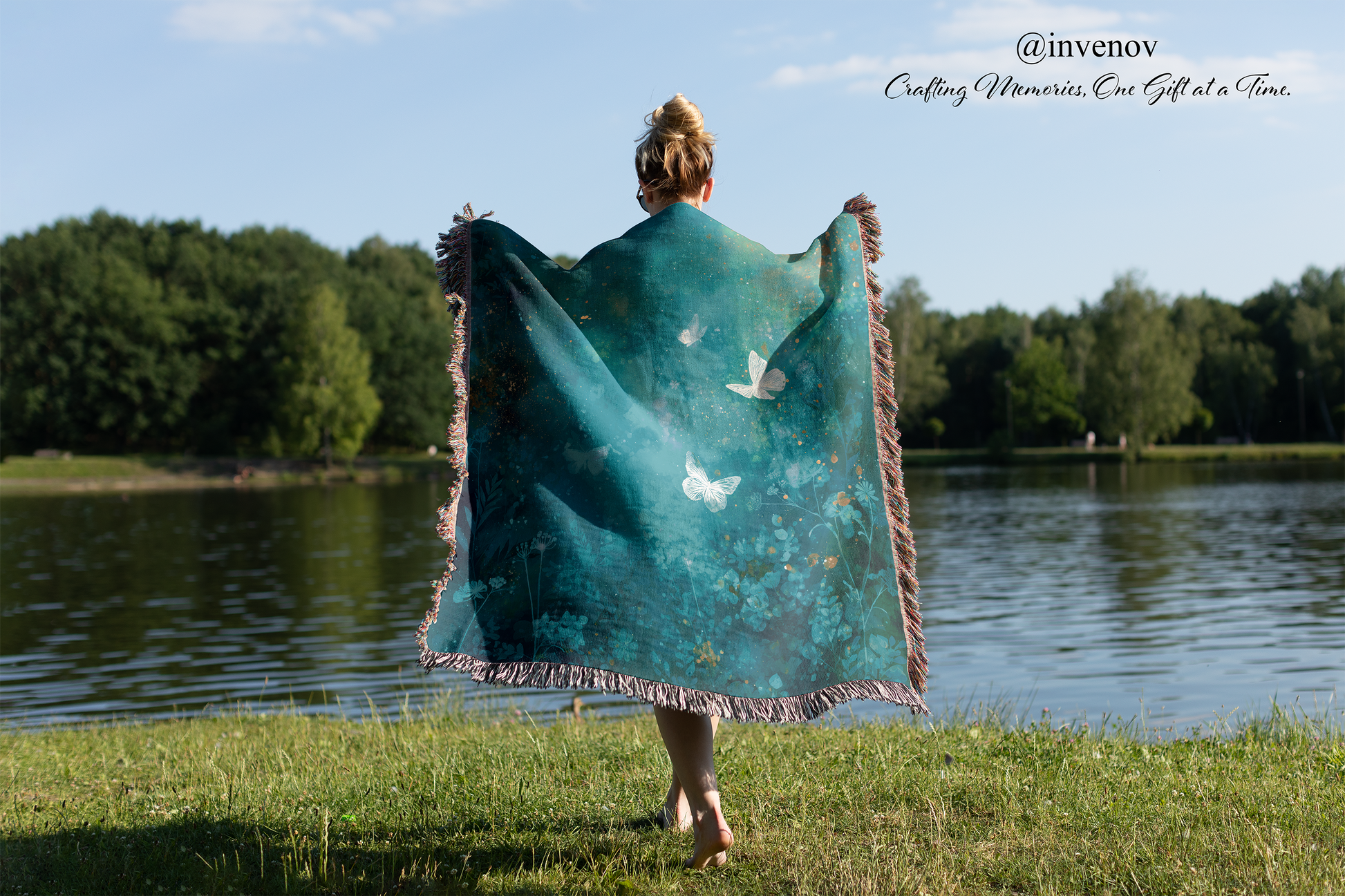 Person holding a teal blanket with fringe, standing by a lake with trees in the background.