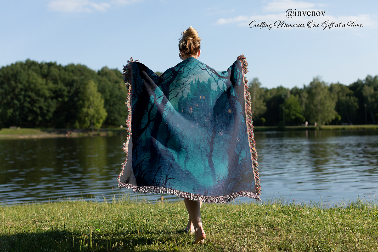 Person holding a large blue and green patterned blanket by a lake with trees in the background.