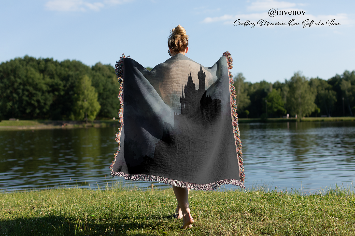 Person holding a blanket with a castle design by a lake, with 'invenov' branding.