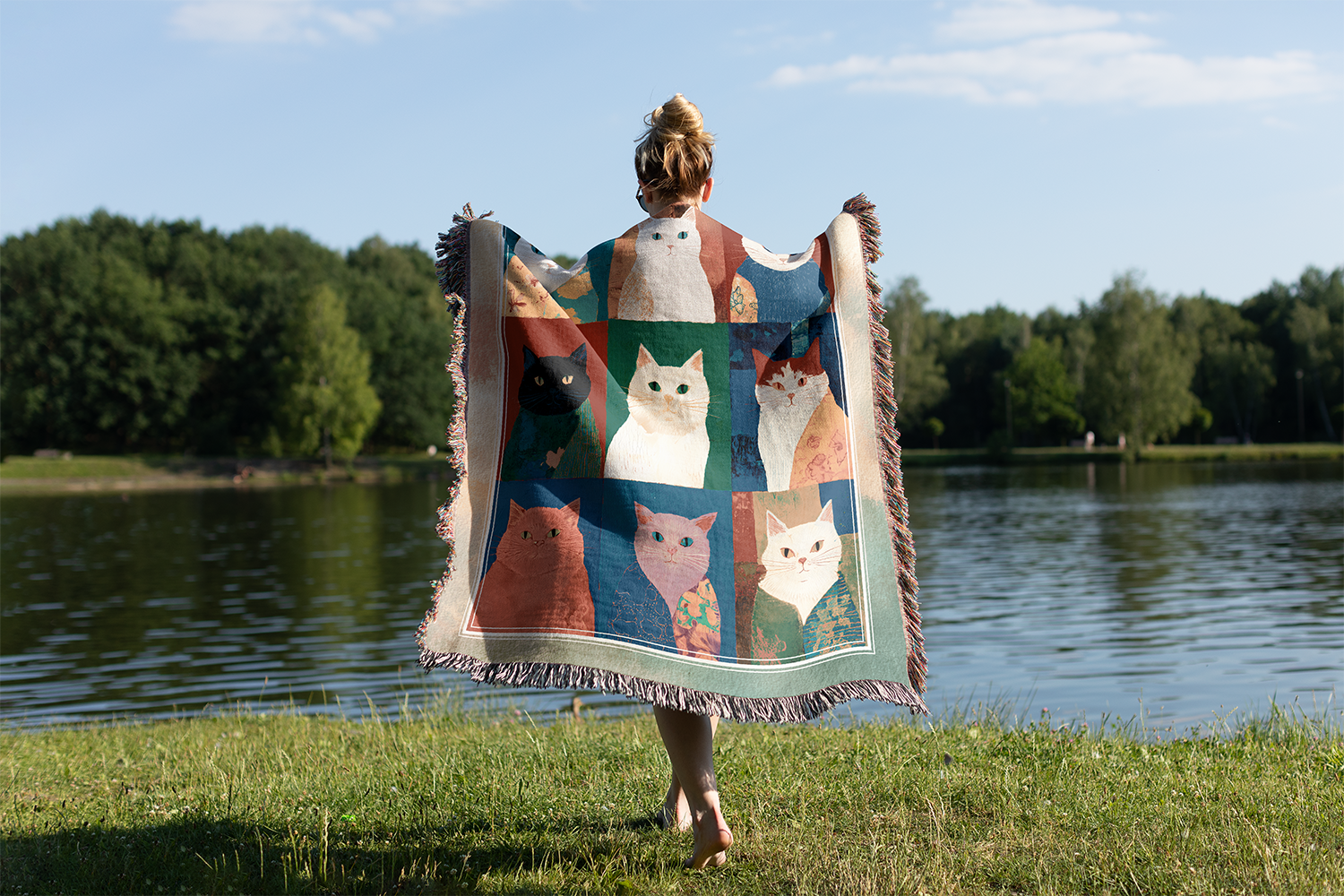 Person holding a colorful blanket with cat patterns by a lake