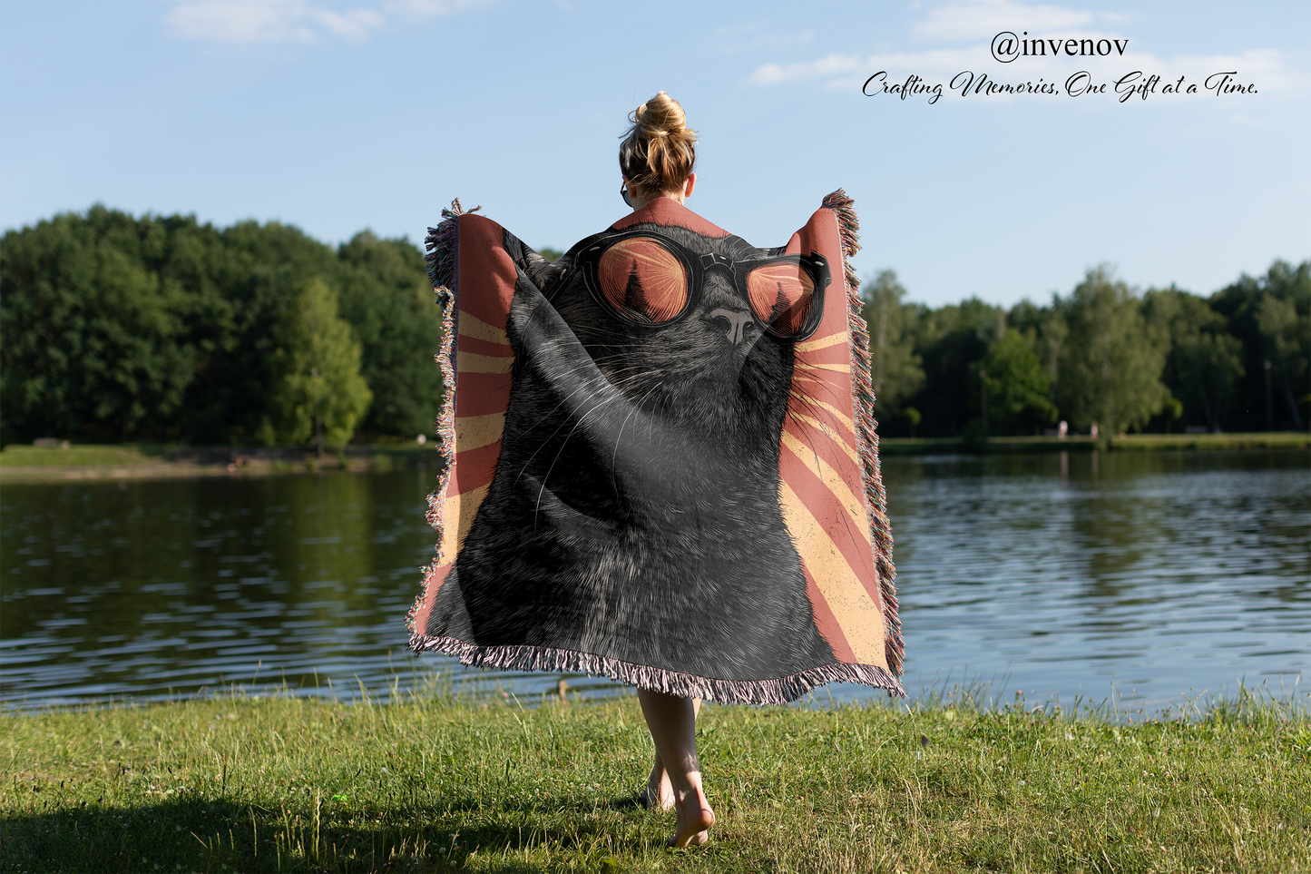 Person holding a large black cat blanket by a lake with trees in the background