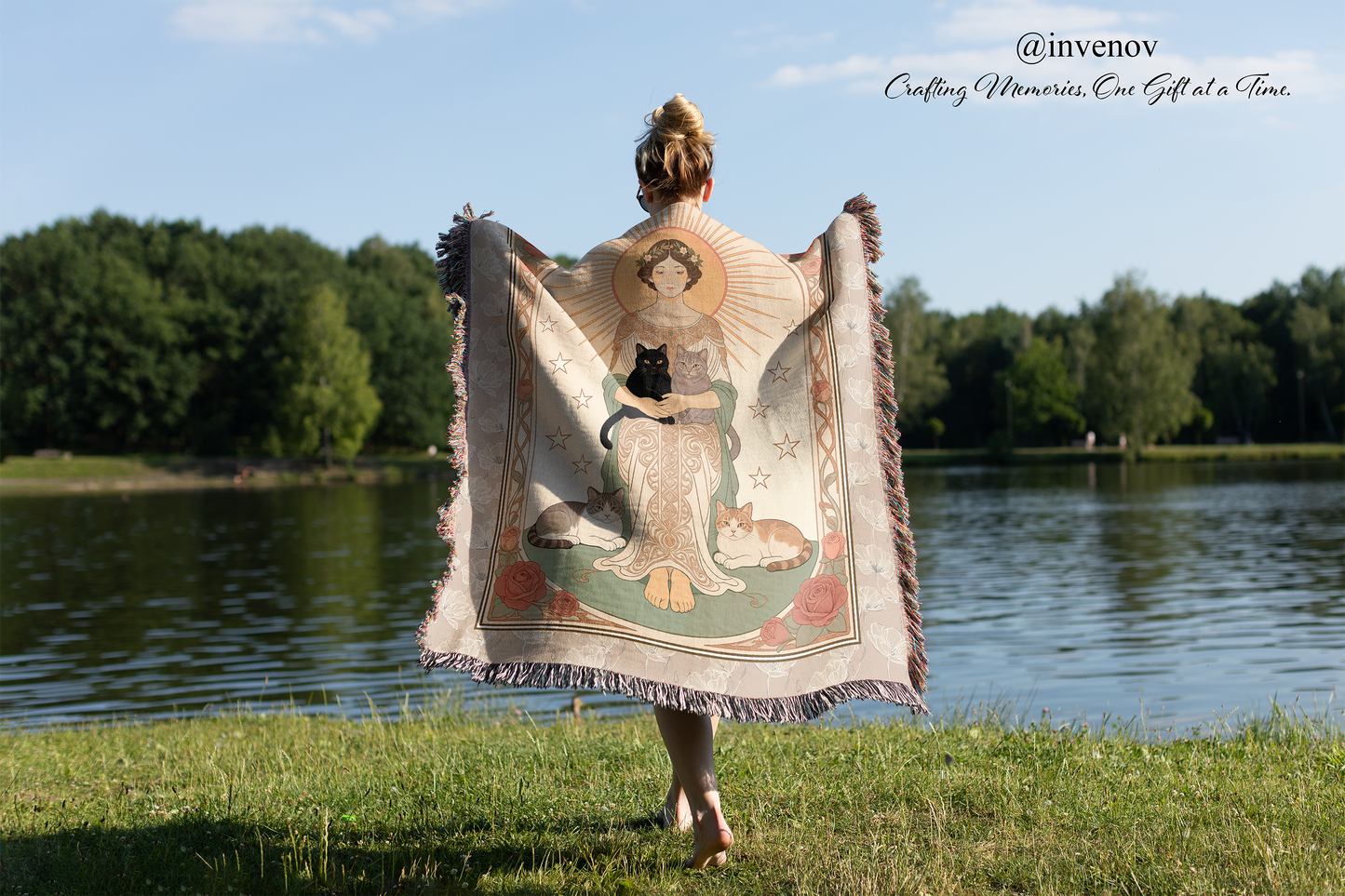 Person holding a decorative blanket with a nature-themed design by a lake