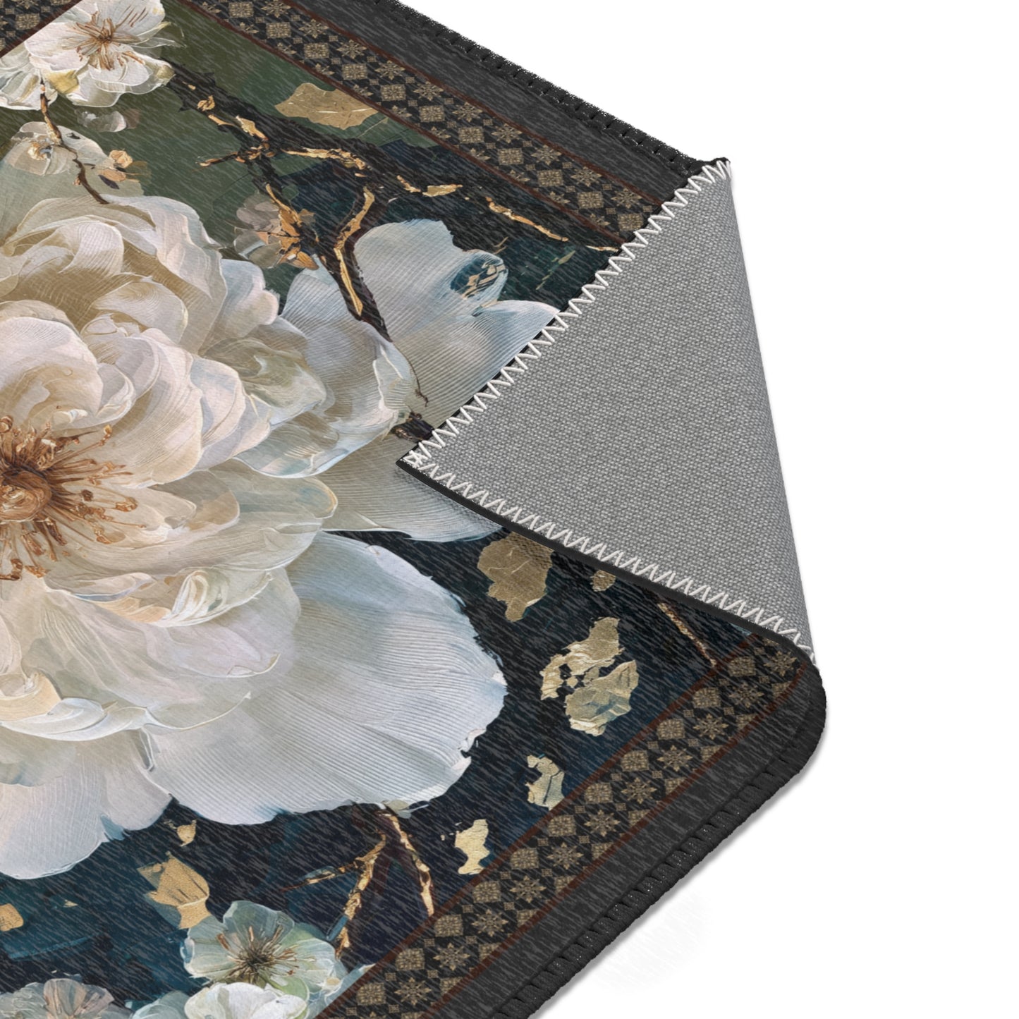 A close-up of a decorative rug or mat showing a large white floral print on a dark navy and black background, with a folded corner revealing a gray textured backing.