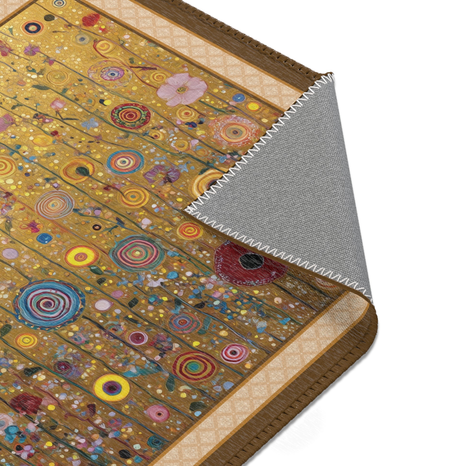 A close-up of a decorative rug or mat with a gold-toned background and many colorful circular and floral motifs, shown with one corner folded back to reveal a gray underside.