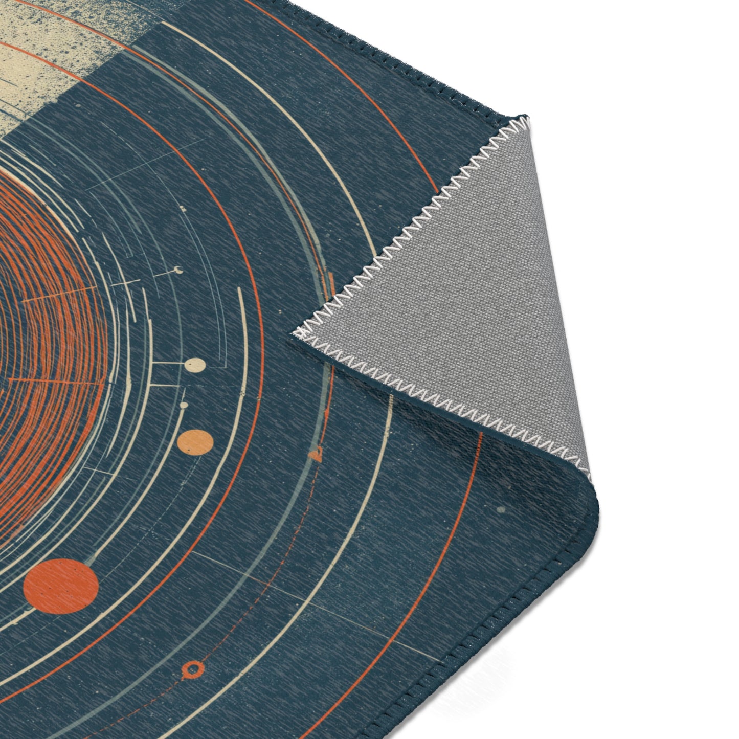 A close-up of a dark blue textured rug with a celestial pattern of orange and cream orbits, with one corner folded over to show the gray backing.