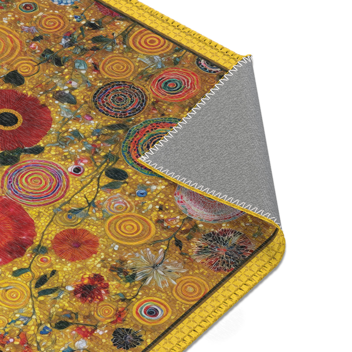 A close-up of a rug with a detailed floral and spiral pattern in warm yellow, red, orange, and green tones, with the corner folded over to show a gray backing.