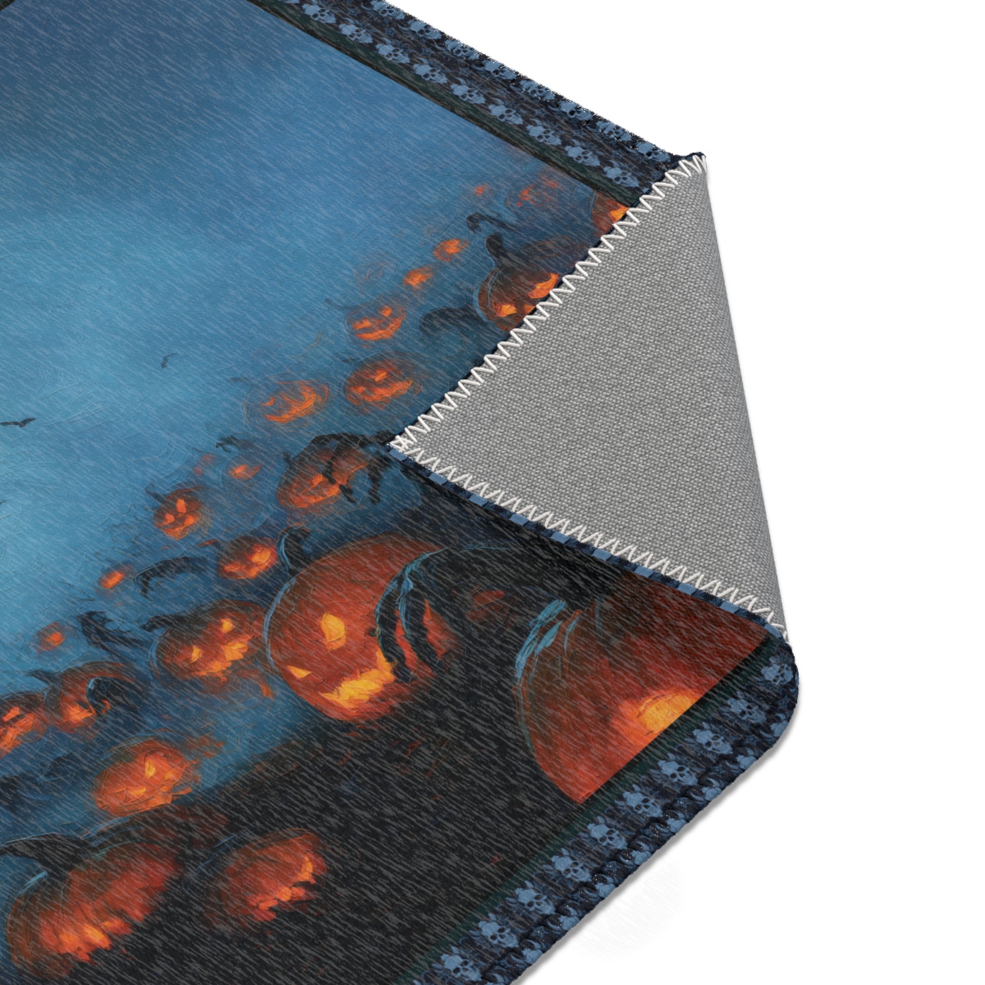 A close-up of a printed rug corner showing a Halloween scene with glowing jack-o'-lantern pumpkins and bats on a blue background, with the underside and stitched edge visible.
