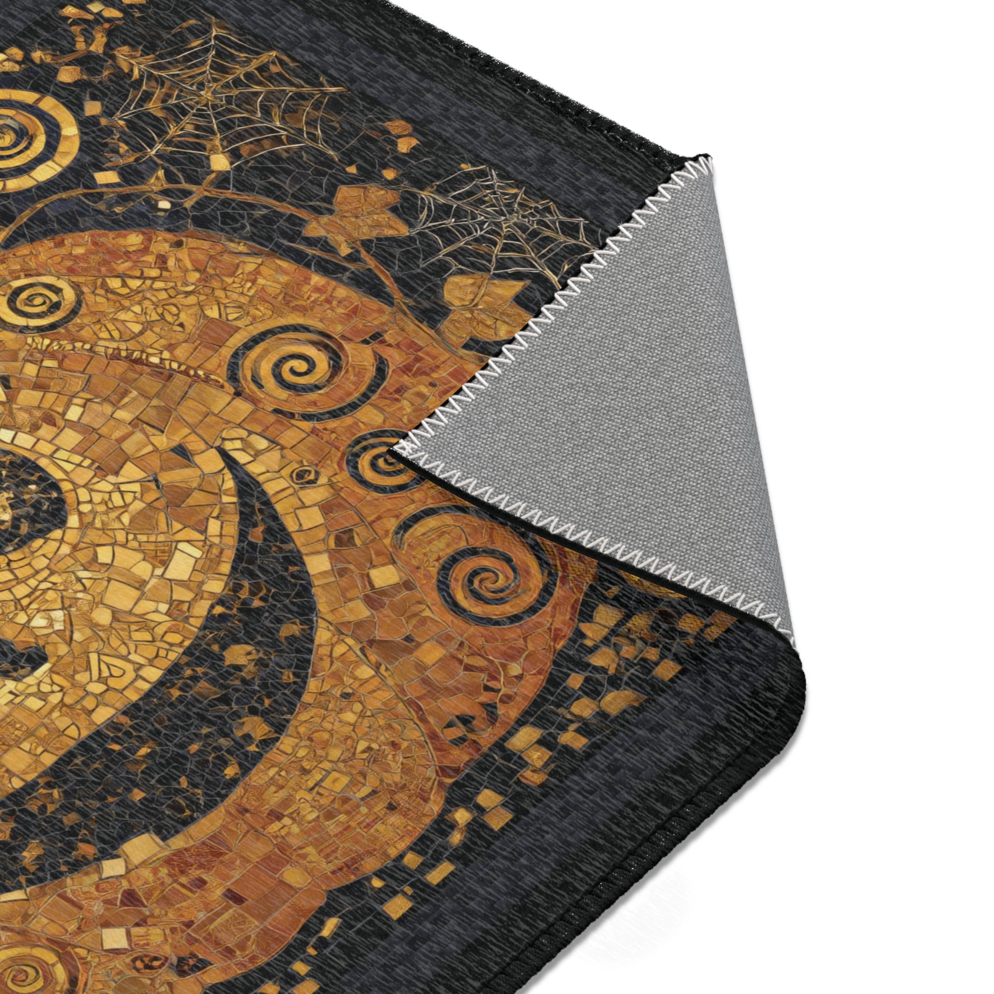 A close-up of area rug featuring a gold and black mosaic art design, with the corner folded over to show a textured gray non-slip backing, set against a plain white background.
