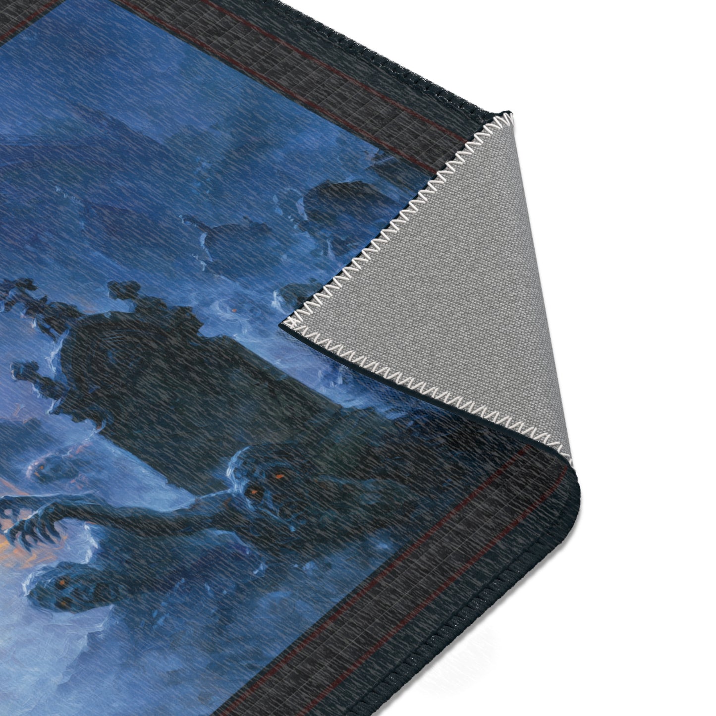 A close-up of a rectangular mat or rug with a printed fantasy scene in blue, black, and gray tones, shown with one corner folded back to reveal a textured gray underside on a white background.