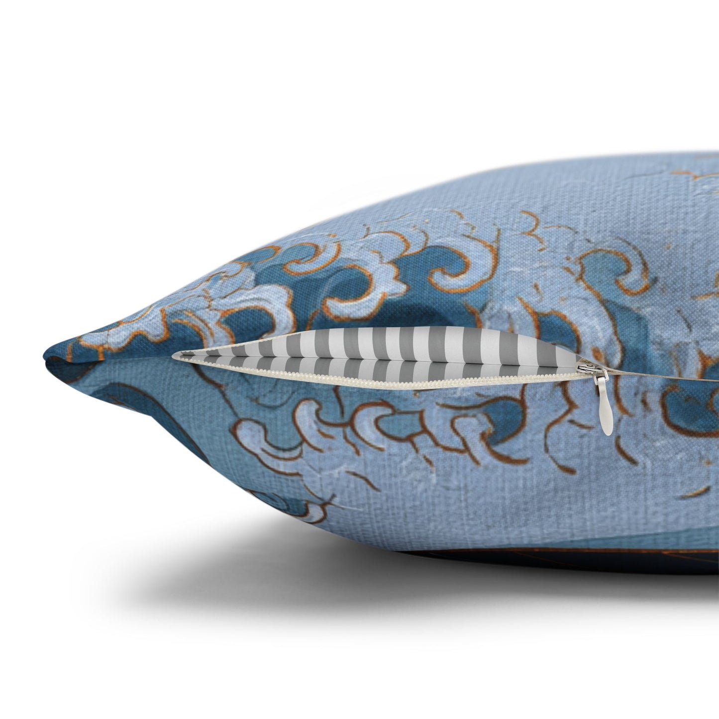 A close-up of a decorative throw pillow with a light blue fabric cover featuring a blue, white, and gold wave pattern, shown with its zipper open to reveal a striped interior.