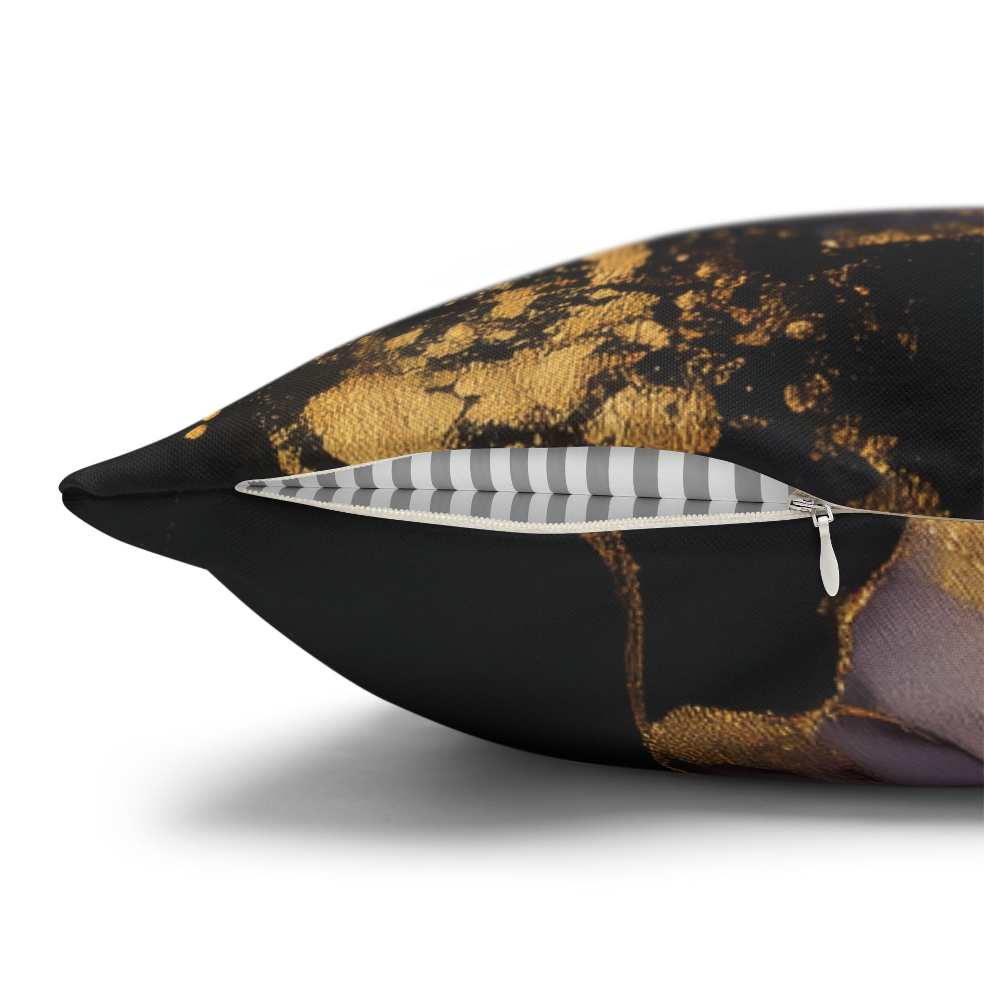 A close-up of a decorative throw pillow with a black and gold abstract marble pattern, showing a striped inner lining and a silver zipper.