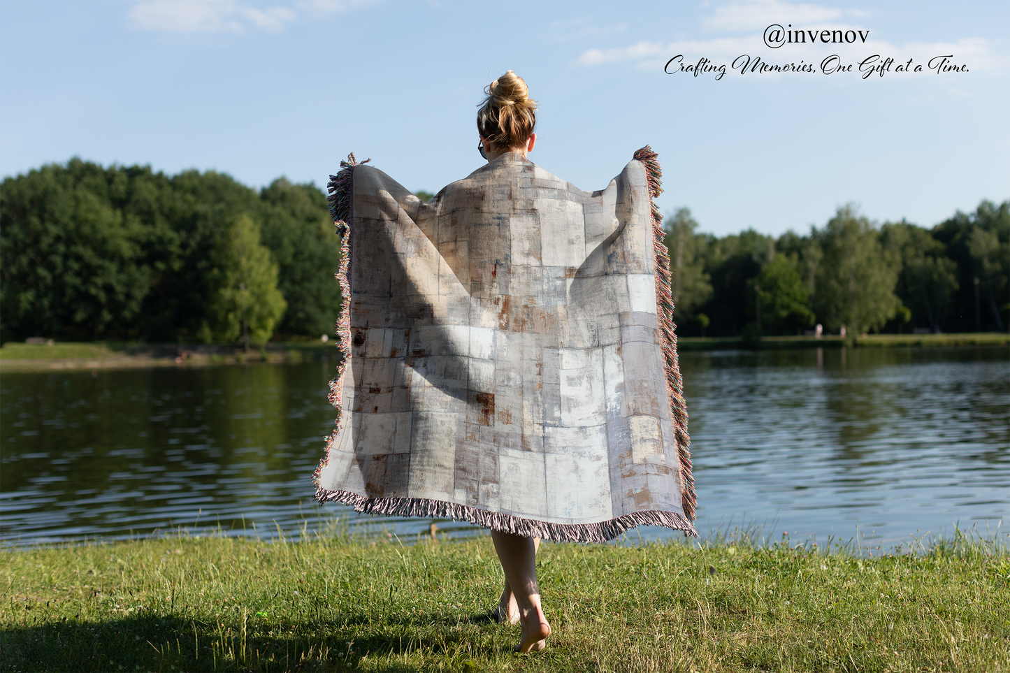 Person holding a large woven blanket by a lake with trees in the background