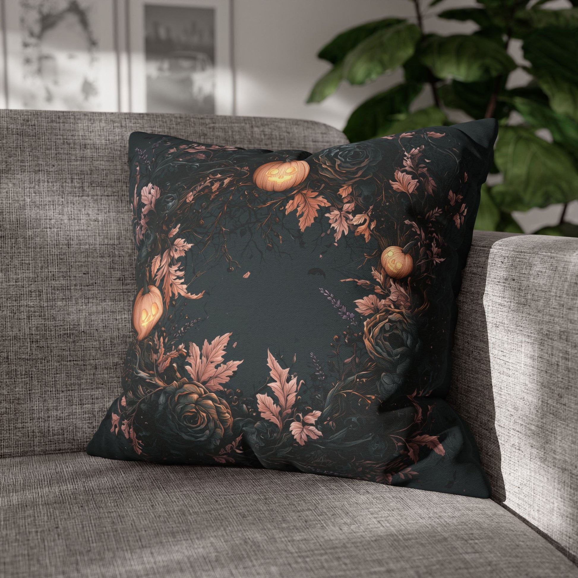 A square throw pillow with a dark gothic floral pattern featuring roses, leaves, and glowing pumpkins, resting on a gray fabric sofa in a living room setting.