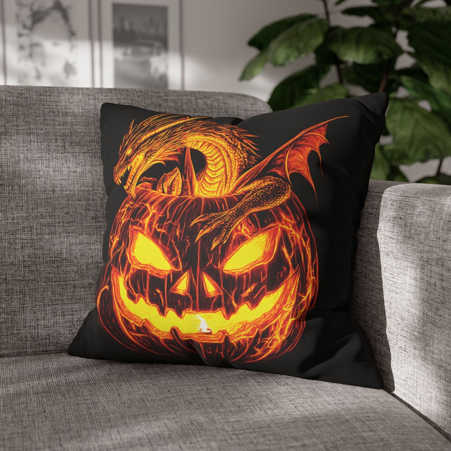 A square black throw pillow featuring a glowing orange and yellow jack-o'-lantern with a dragon wrapped around it, resting on a gray fabric sofa in a home setting.