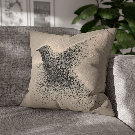 A square throw pillow with a black bird silhouette made of tiny dots on a beige background, resting on a gray textured sofa in a sunlit room with a green plant in the background.