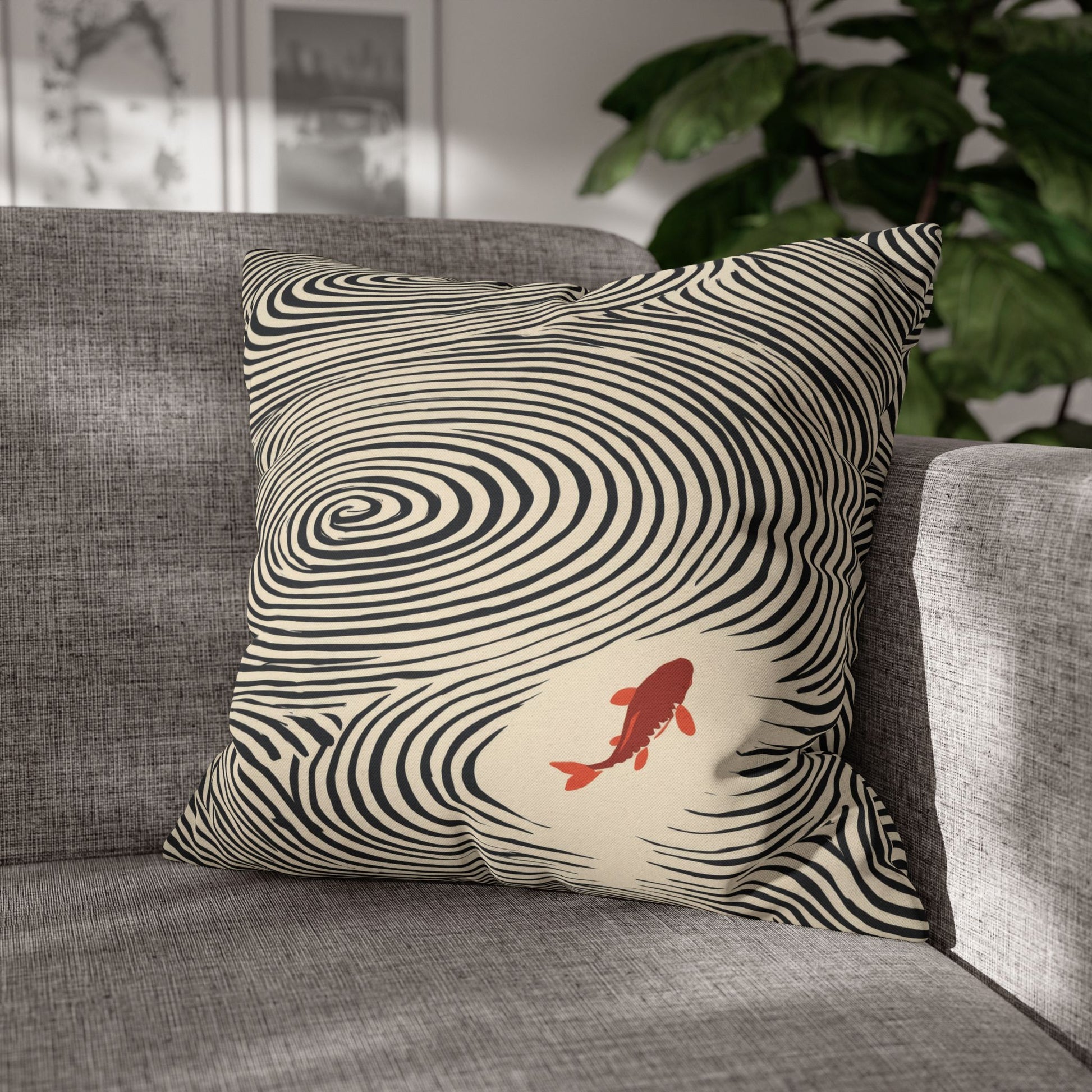 A square throw pillow with a blue and cream wavy optical illusion pattern and a red koi fish, resting on a gray fabric sofa in a living room setting.