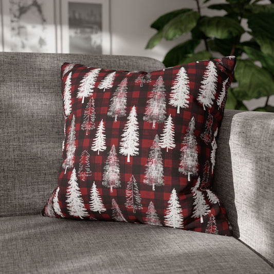 A square throw pillow with a red and black buffalo plaid pattern overlaid with white pine tree silhouettes, resting on a gray fabric sofa with a blurred indoor background.