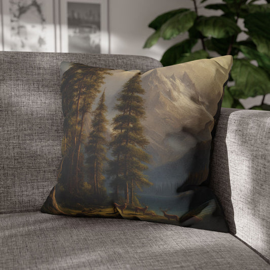 A square throw pillow featuring a scenic landscape print of pine trees, mountains, and deer, styled on a gray textured sofa in a living room setting.