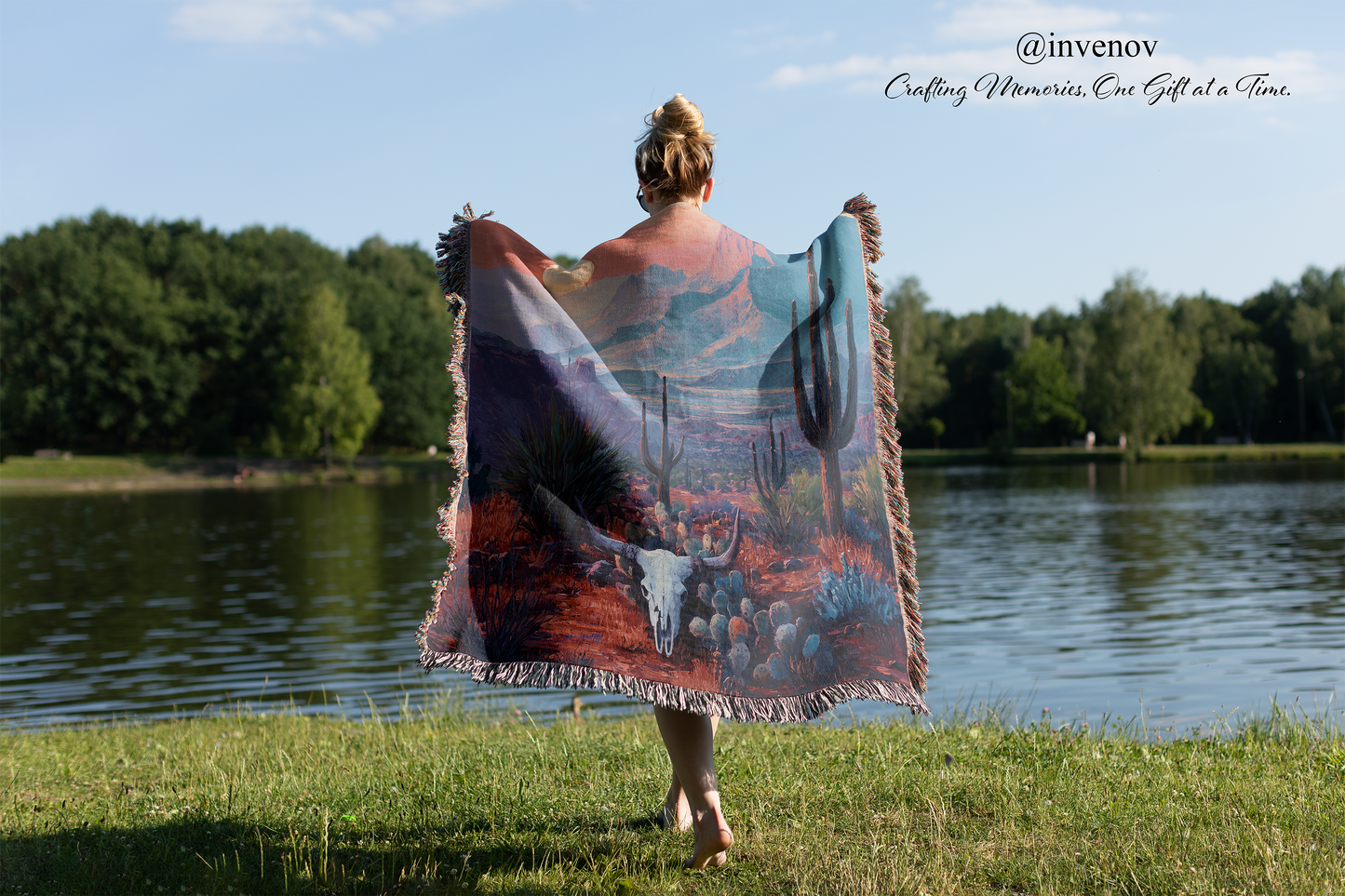 Person standing by a lake with a colorful blanket draped over them, featuring nature-themed designs.