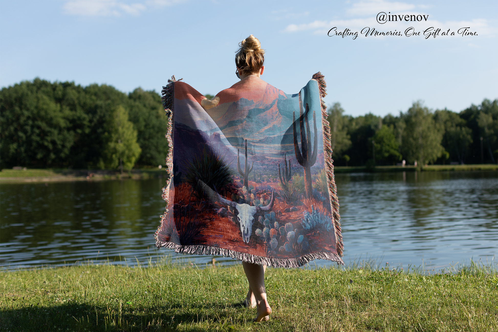 Person standing by a lake with a colorful blanket draped over them, featuring nature-themed designs.