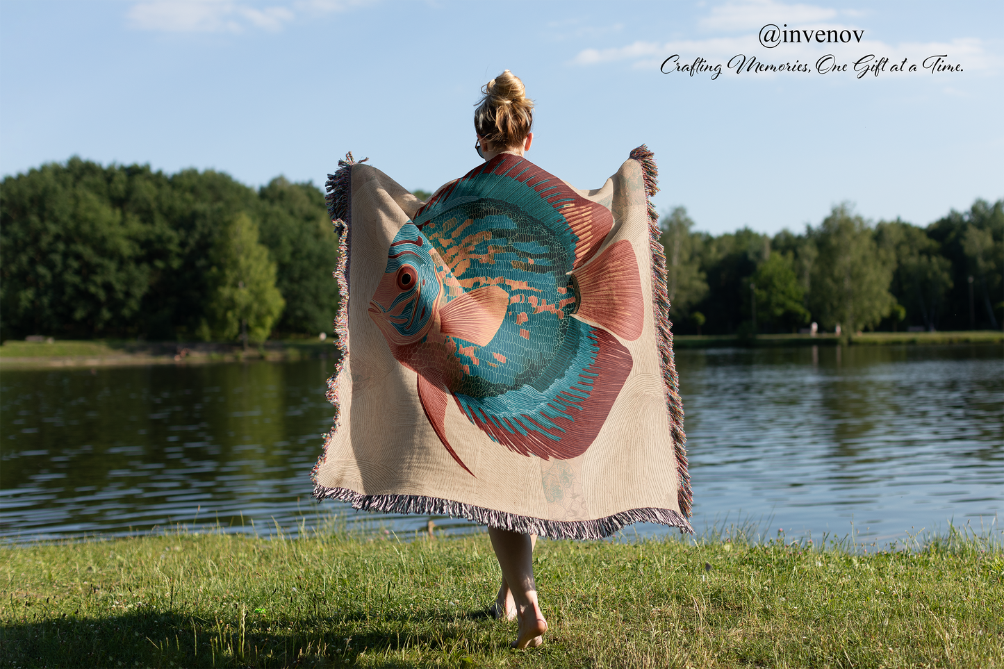 Person holding a colorful fish-patterned towel by a lake 