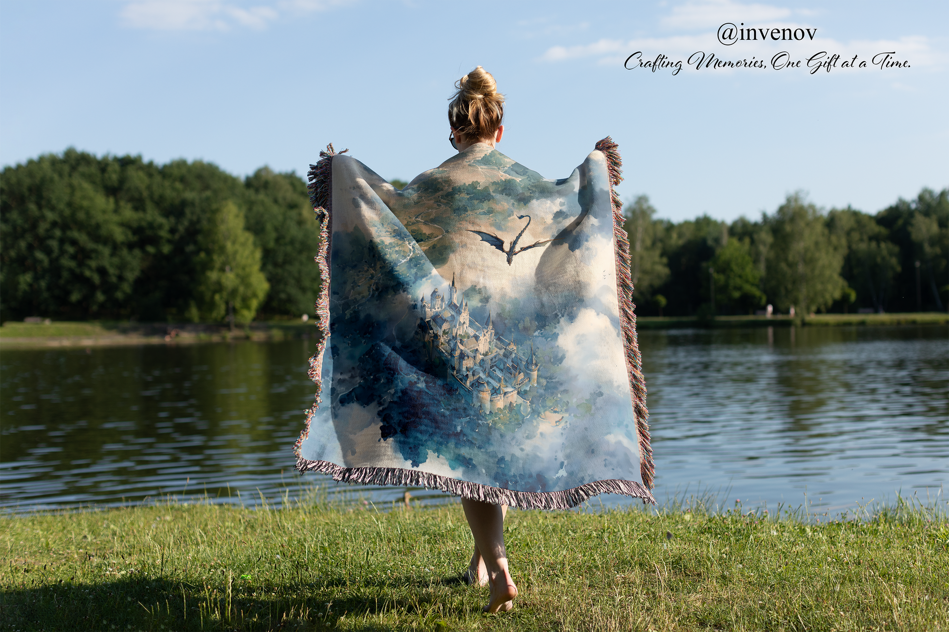Person holding a large blanket with a nature design by a lake, with 'invenov' branding.