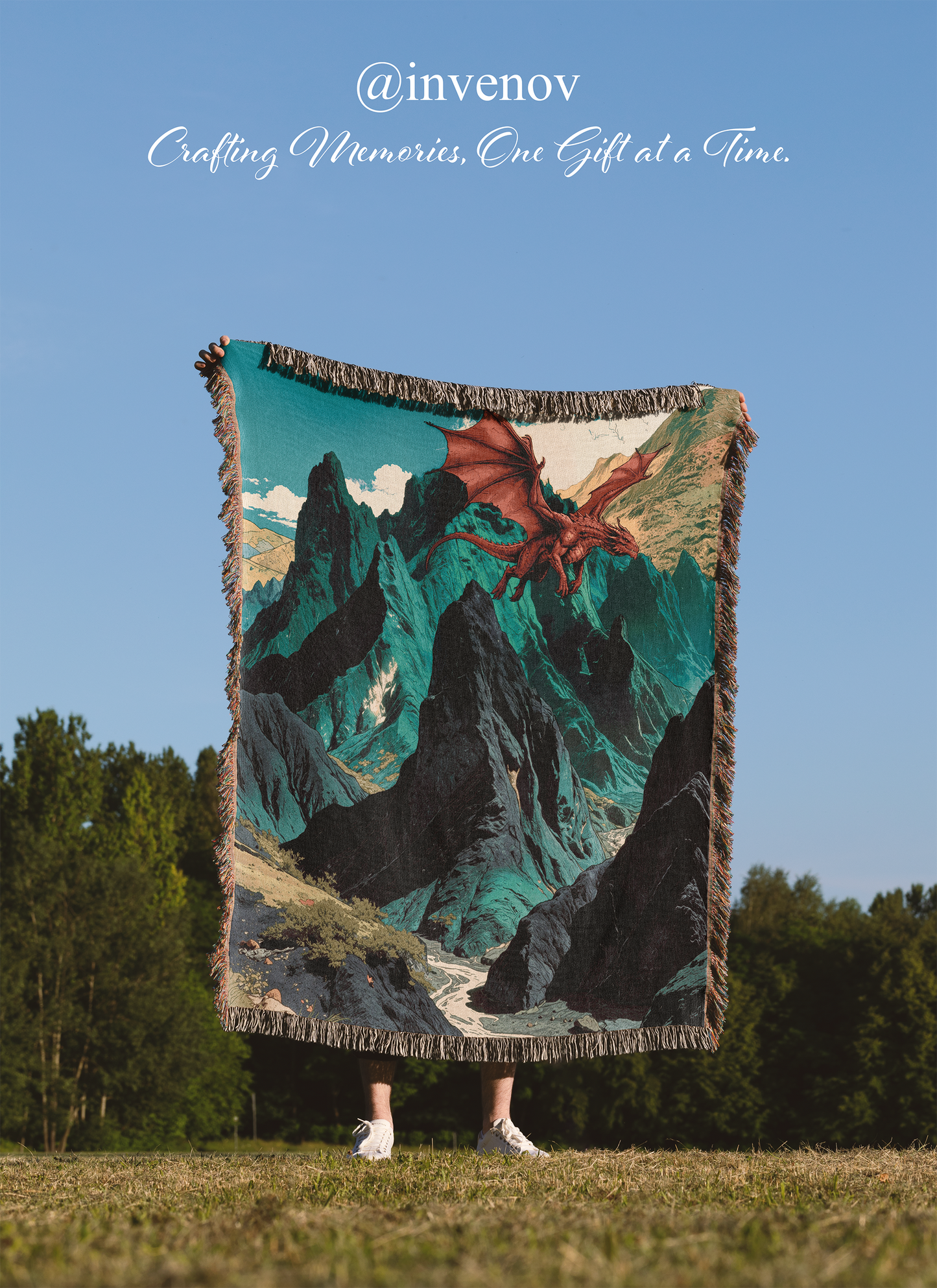 Person holding a large woven blanket with a mountain and dragon design in an outdoor setting.