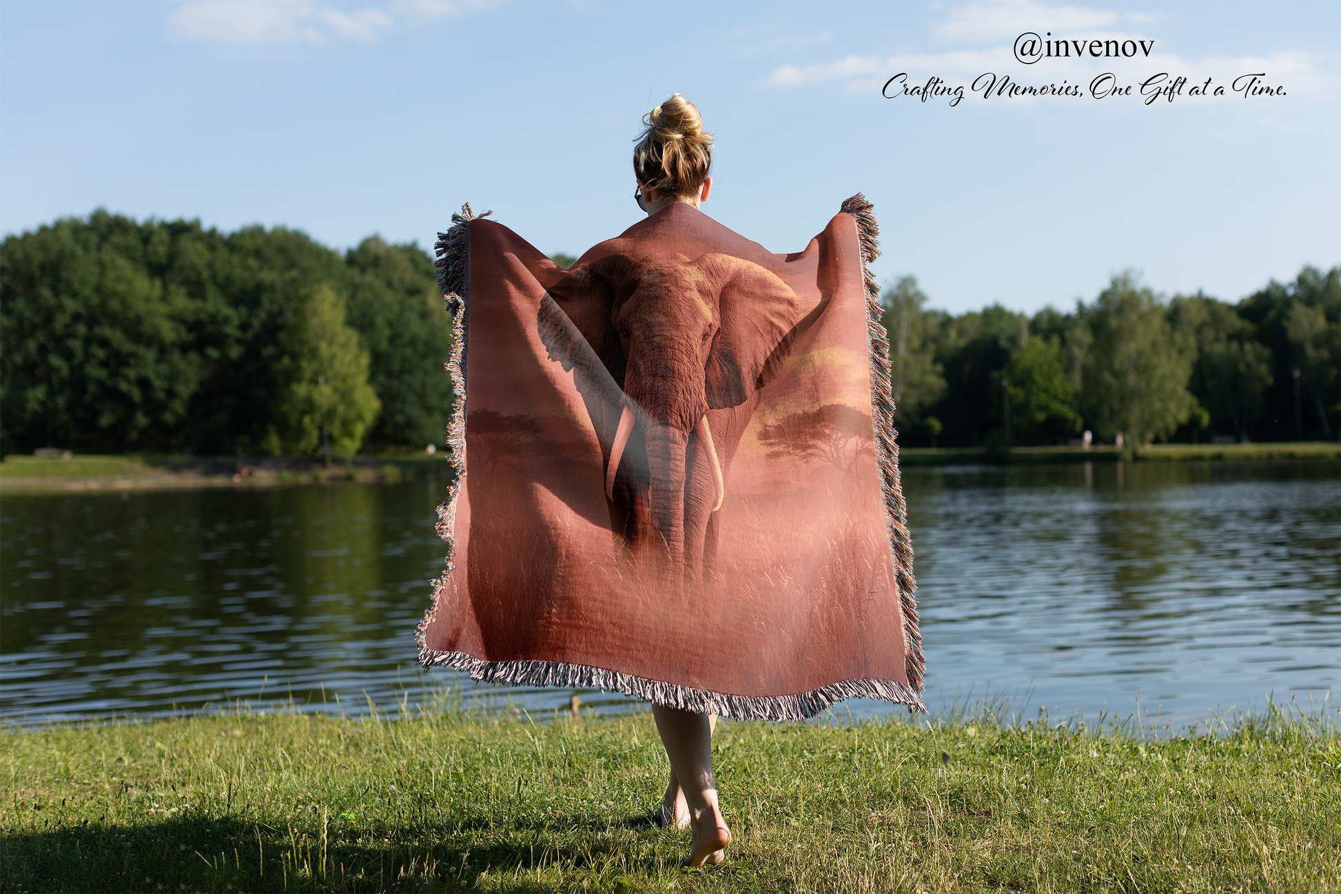 Person holding a elephant-patterned blanket by a lake with trees in the background