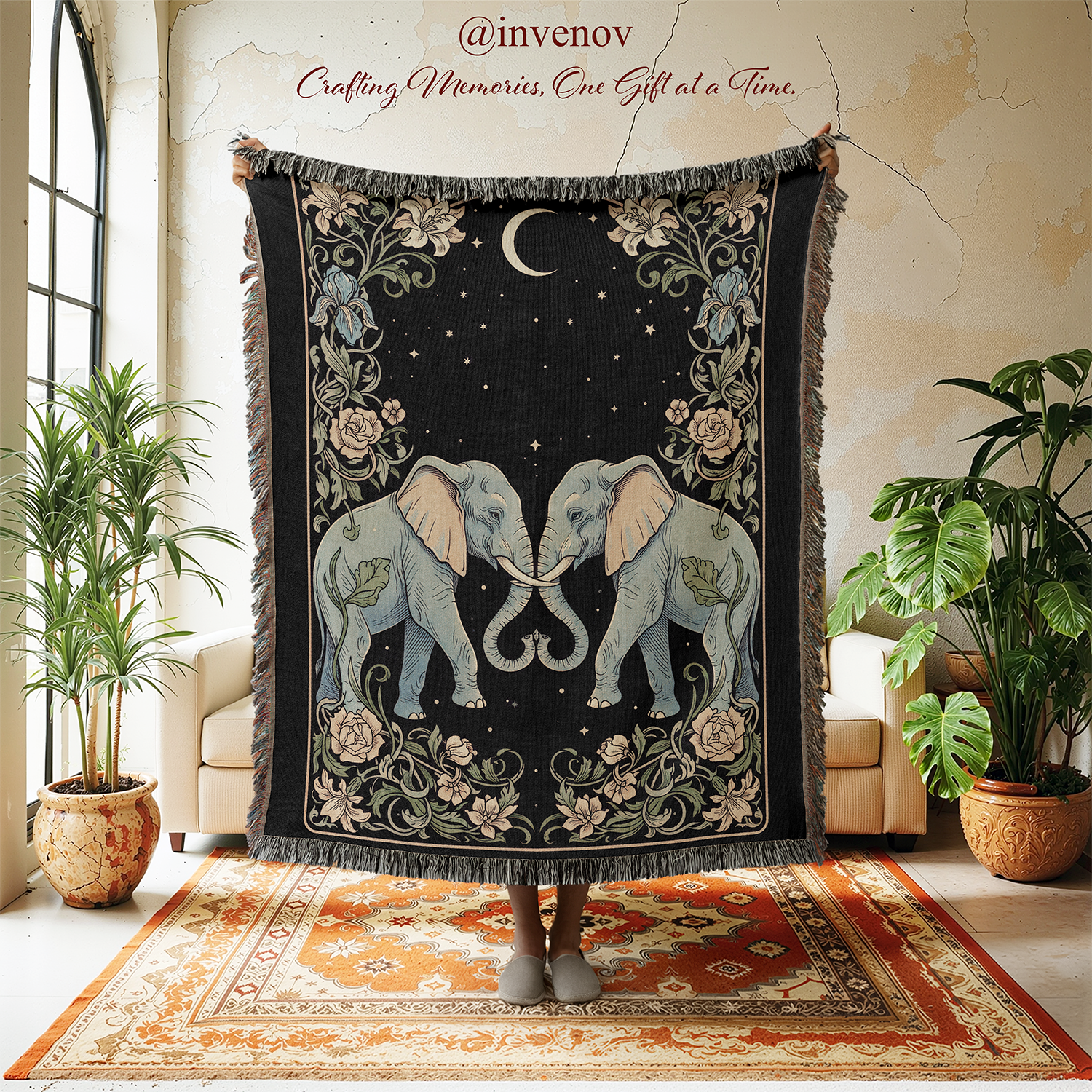 Decorative throw blanket with elephant design held by a person in a room with plants and furniture.