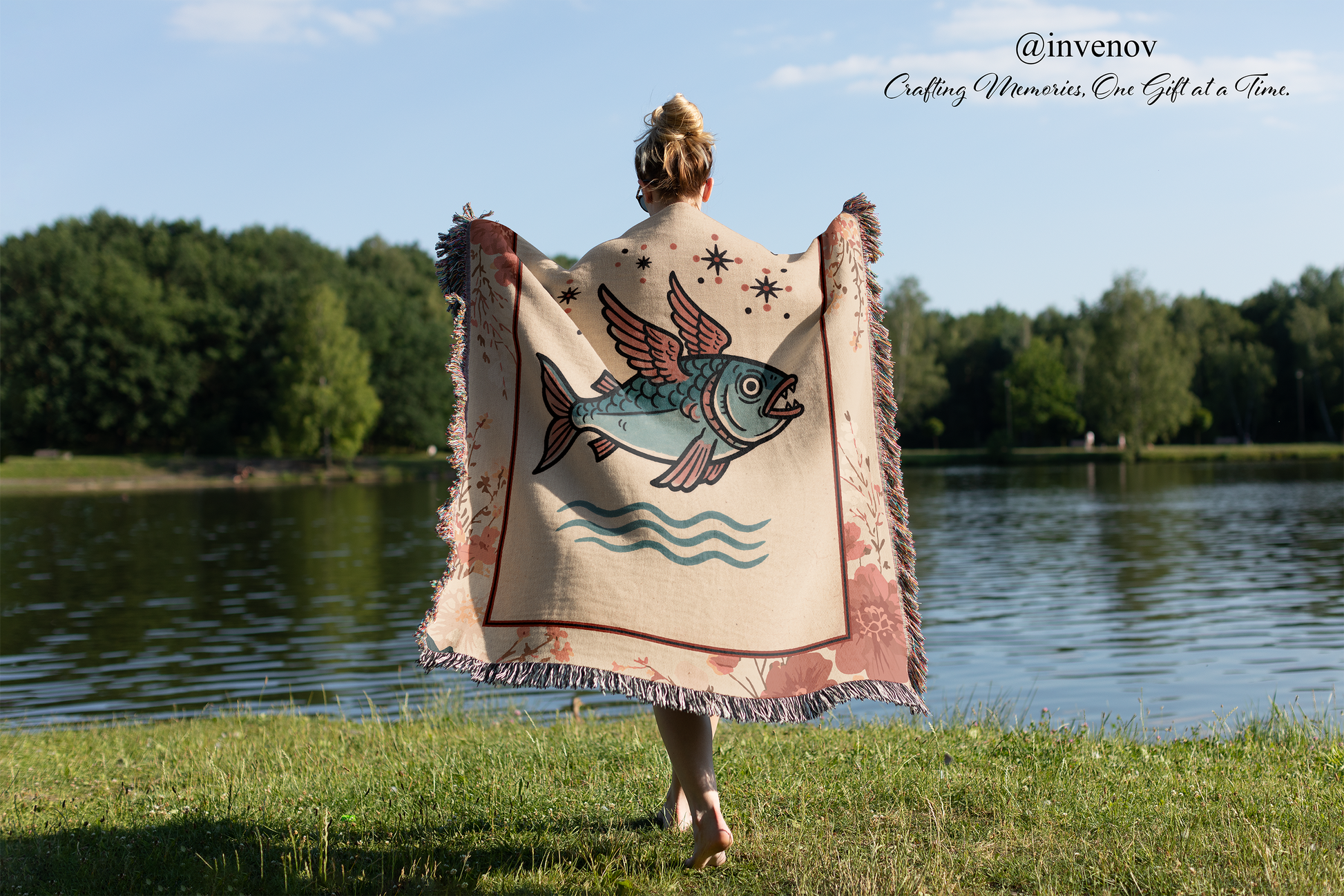 Person holding a decorative blanket with a fish design by a lake