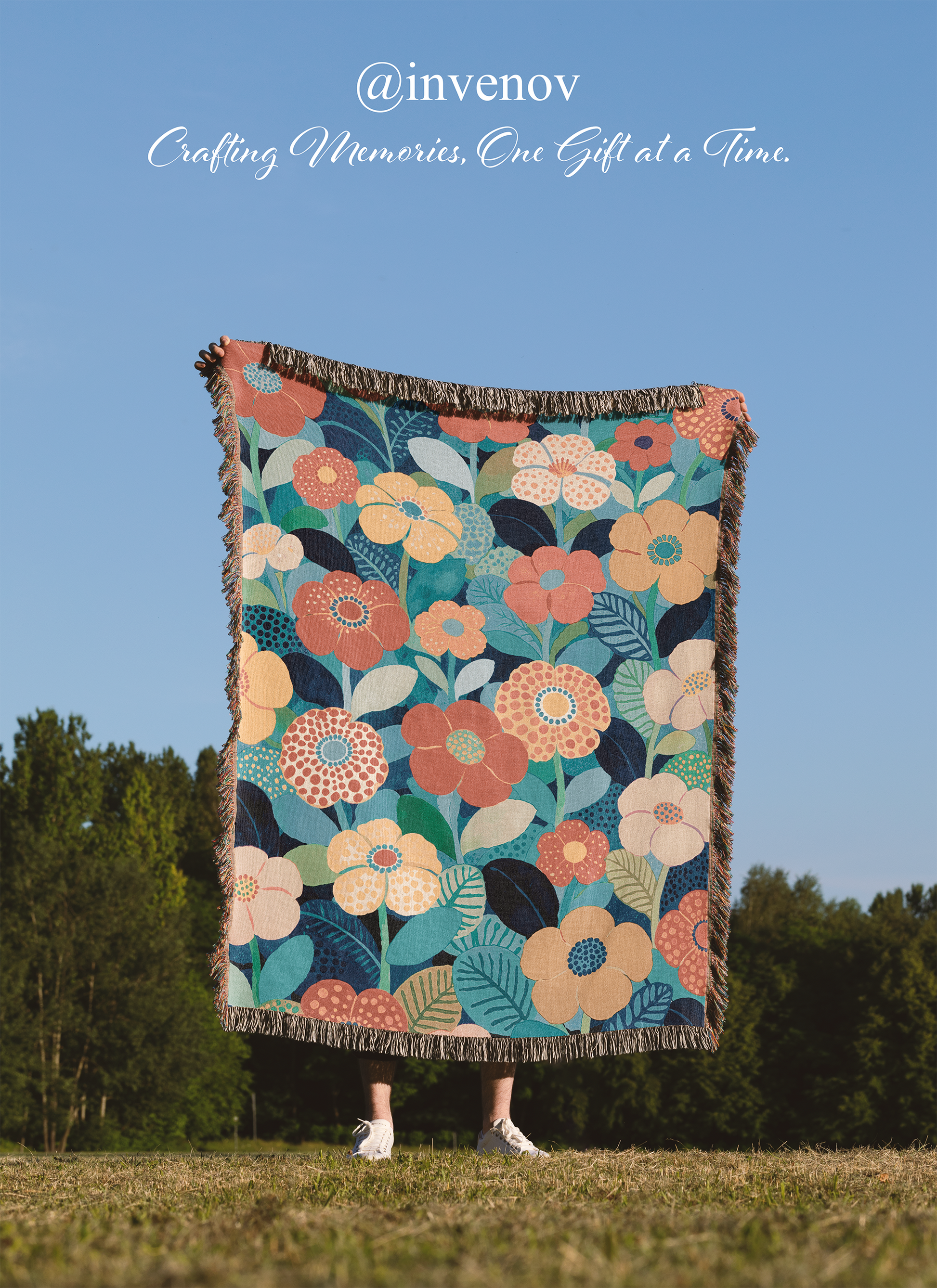 Colorful floral-patterned blanket being held up outdoors with a clear blue sky and trees in the background.