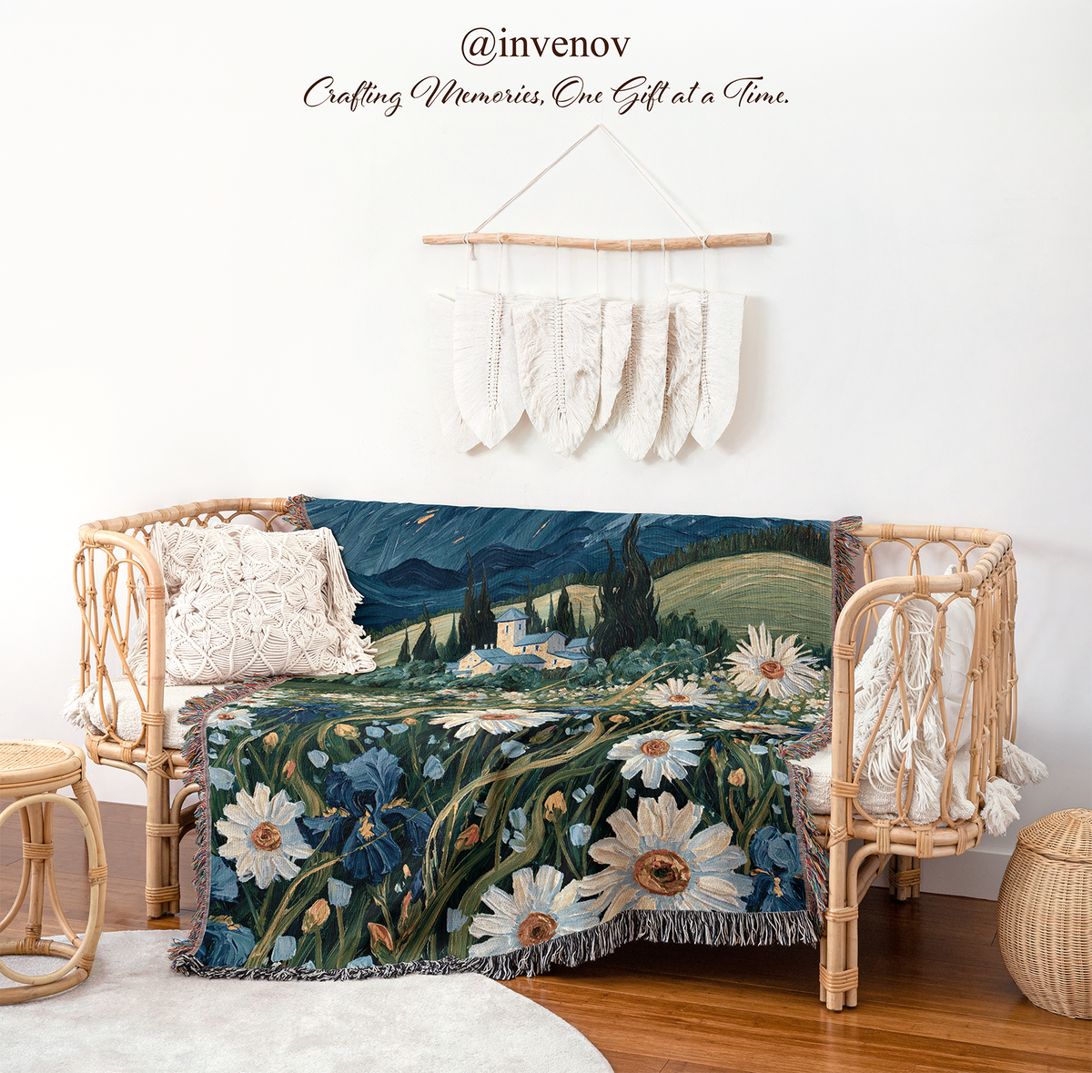 A woven tapestry throw blanket featuring a floral landscape design with daisies and blue flowers, draped over a rattan daybed in a styled room setting.
