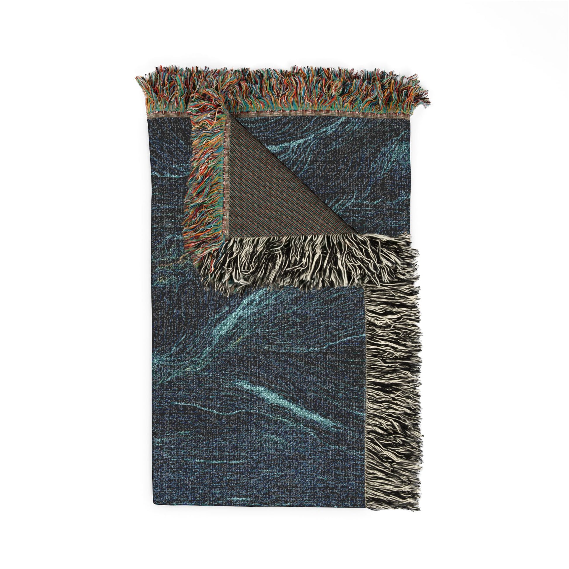 A rectangular woven throw blanket with multicolored fringe, featuring a dark blue and teal abstract pattern with a folded corner revealing a brown backing.