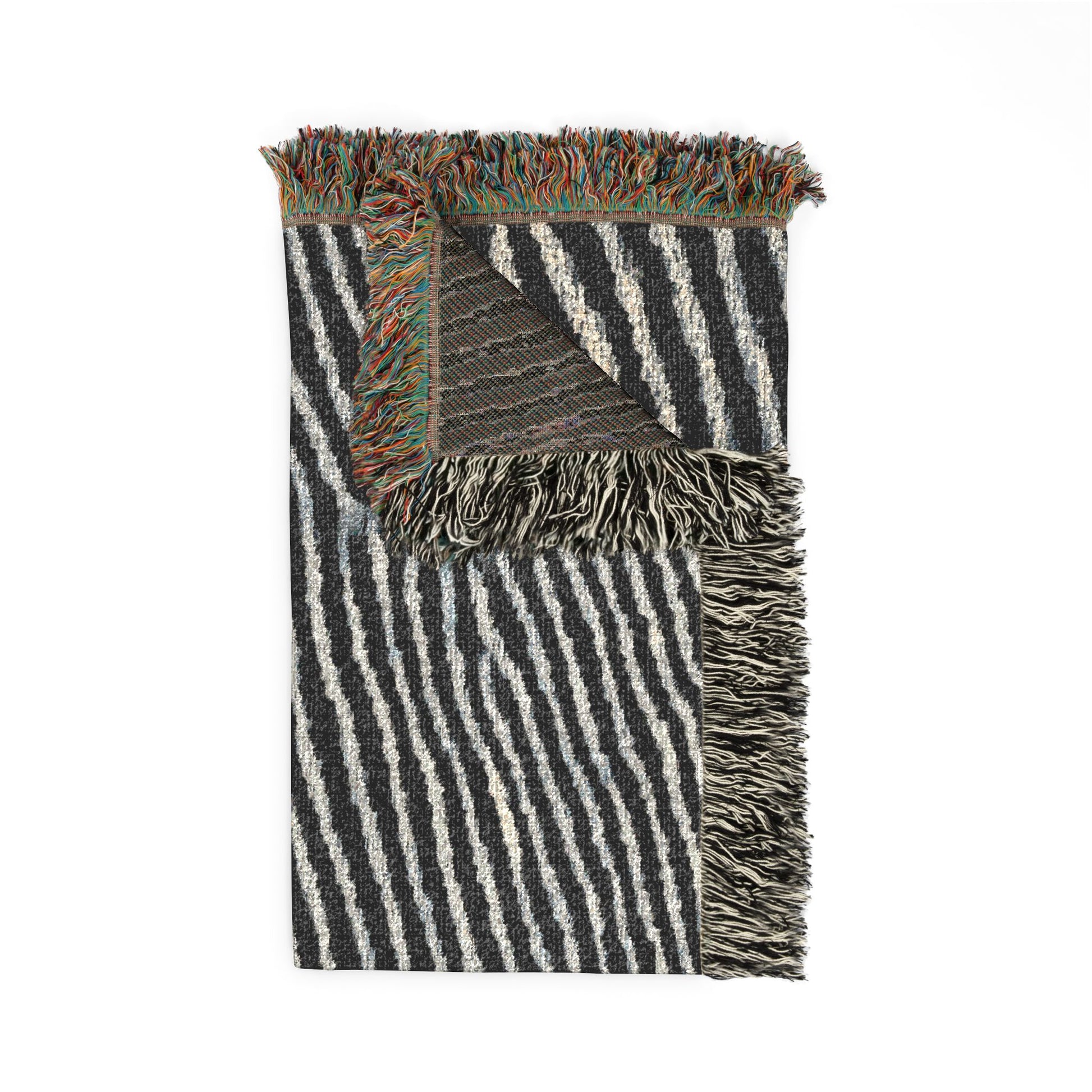 A folded woven throw blanket with black and off-white vertical stripes, featuring multicolor fringed edges and a textured geometric pattern on the reverse side, shown on a plain white background.