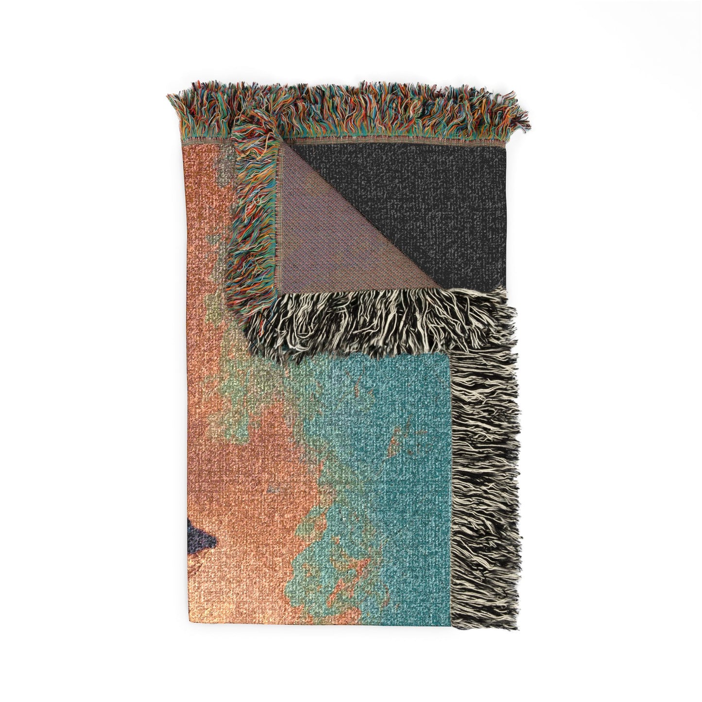 A folded woven throw blanket with multicolor abstract patterns in teal, terracotta, and charcoal, finished with fringed edges and a dark backing, shown on a plain white background.