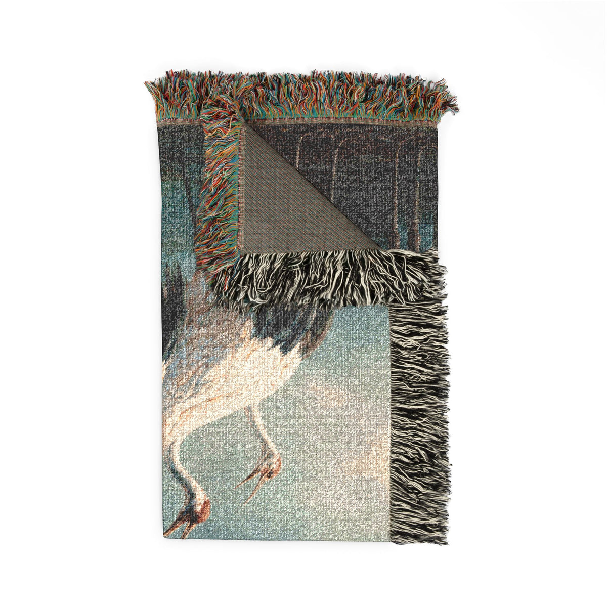 A woven throw blanket featuring a detailed print of a heron, with multicolored fringe on all sides and a solid textured gray backing visible on one corner, shown against a plain white background.