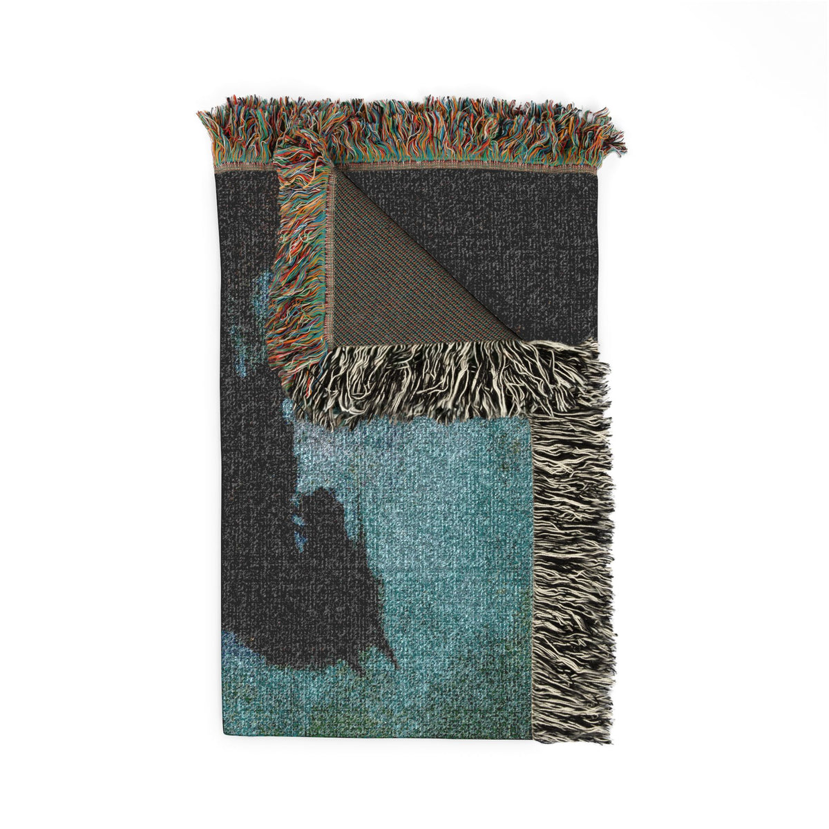 A folded woven throw blanket with multicolored fringe, featuring a dark charcoal gray and teal abstract pattern on a white background.