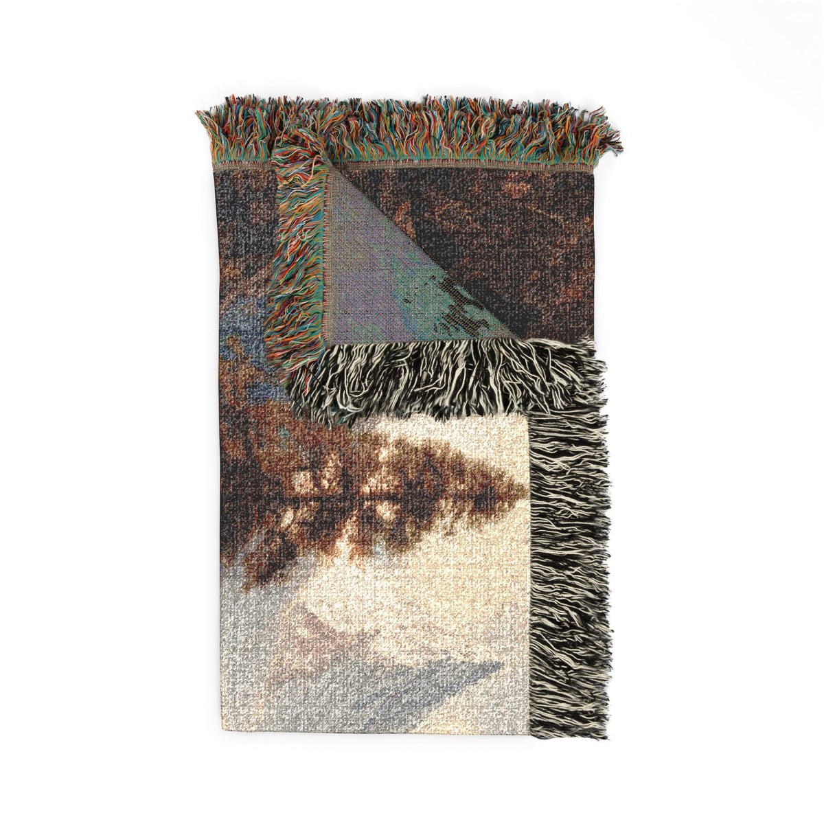 A rectangular woven throw blanket with fringed edges, featuring an abstract landscape-like pattern in earthy tones of brown, beige, gray, and muted blue-green. One corner is folded over to show the reverse side and fringe detail, photographed on a plain white background.