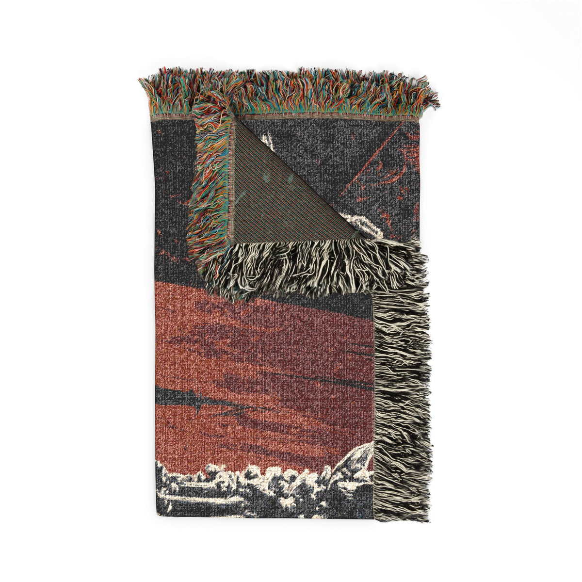 A folded woven throw blanket with multicolor fringe, featuring a geometric pattern in rust red, black, gray, and white.