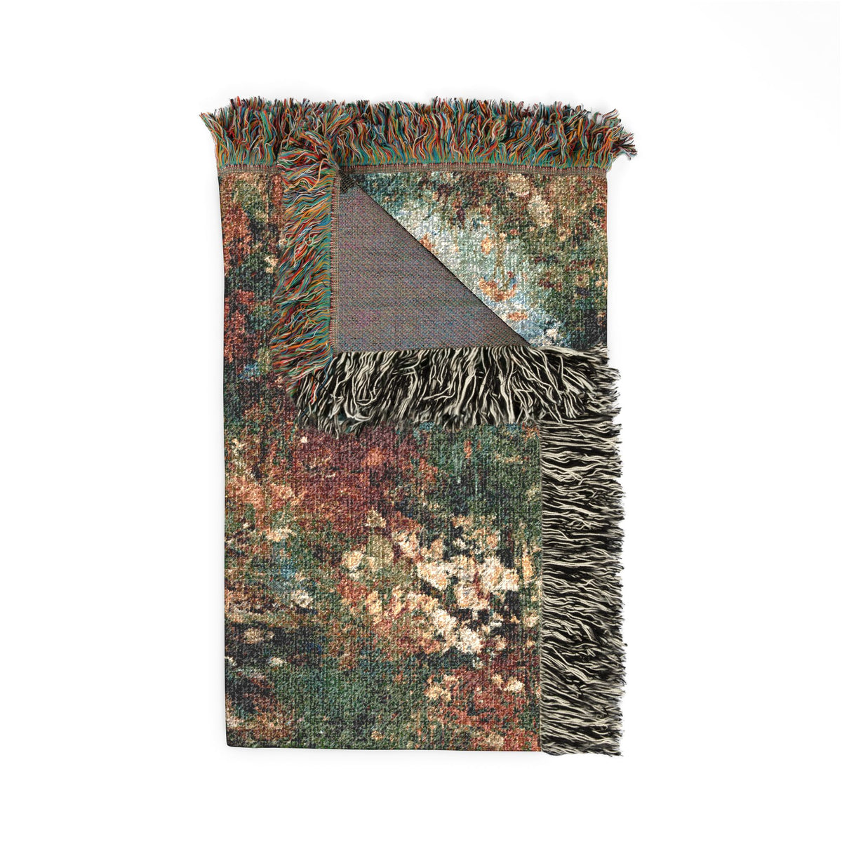 A rectangular woven throw blanket with fringed edges, featuring a distressed multicolor pattern in green, brown, orange, and cream, with a solid dark gray reverse side visible at the folded corner.
